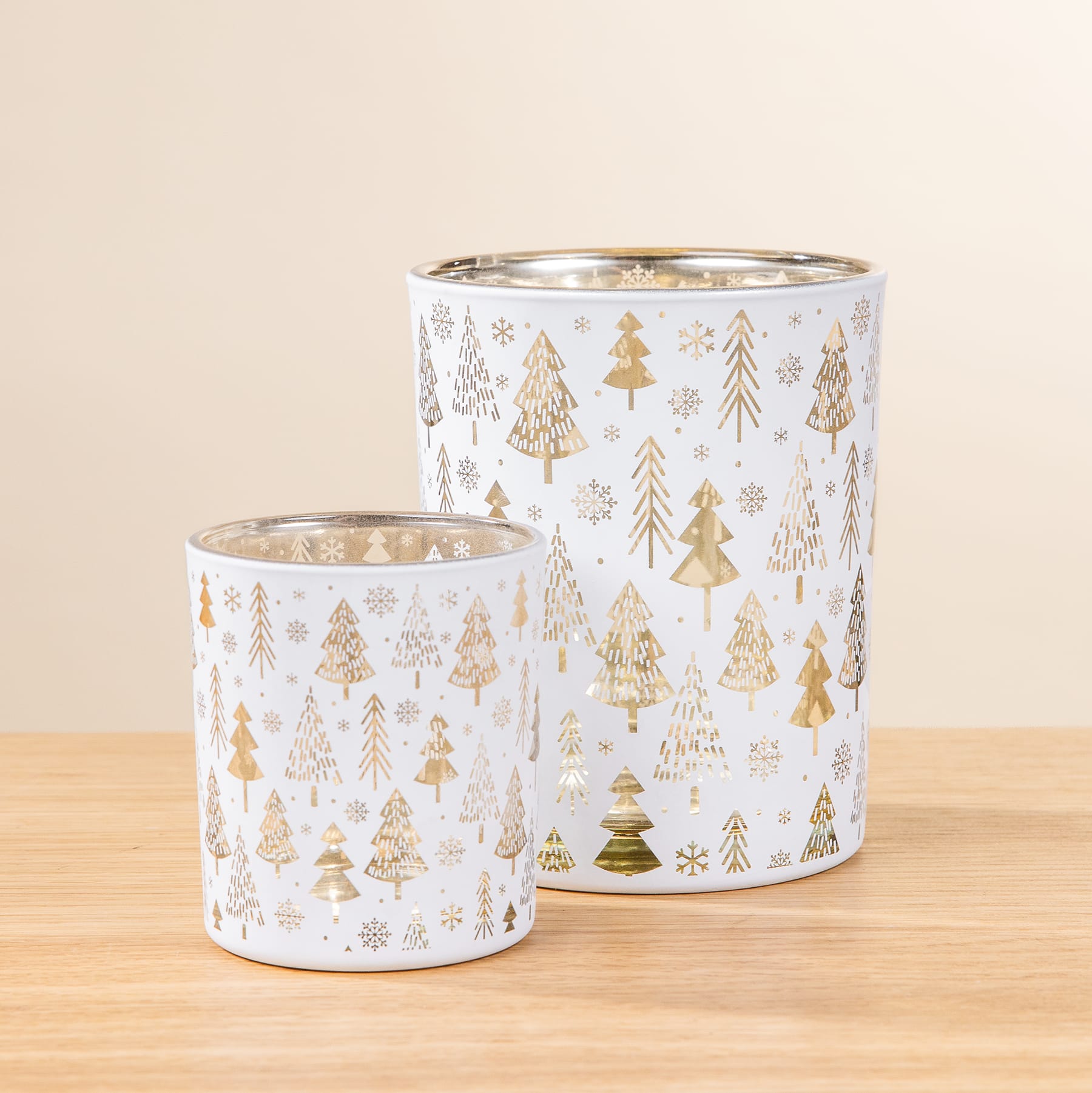 Zwei Kerzenhalter aus Glas mit einem weiß-goldenen Weihnachtsbaummuster auf einem Holztisch.