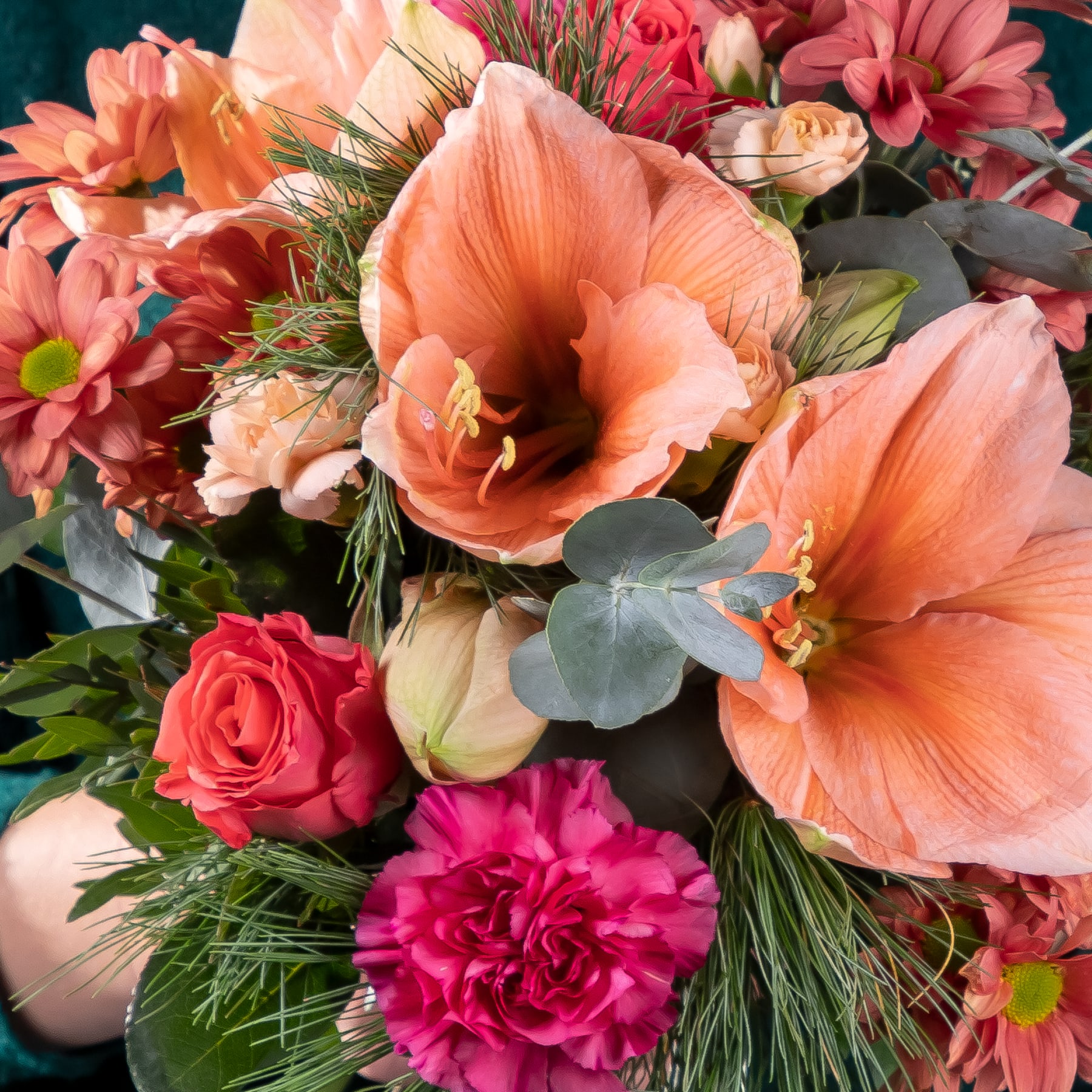 Ein farbenfroher Strauß verschiedener Blumen, darunter großer orangefarbener Hibiskus, rosa Nelken und rote Rosen, vor einem dunklen Hintergrund.