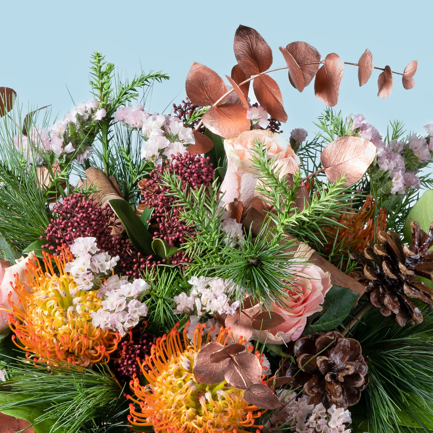 Ein farbenfroher Strauß verschiedener Blumen, darunter Rosen, Chrysanthemen und Tannenzweige, vor einem klaren blauen Himmel.