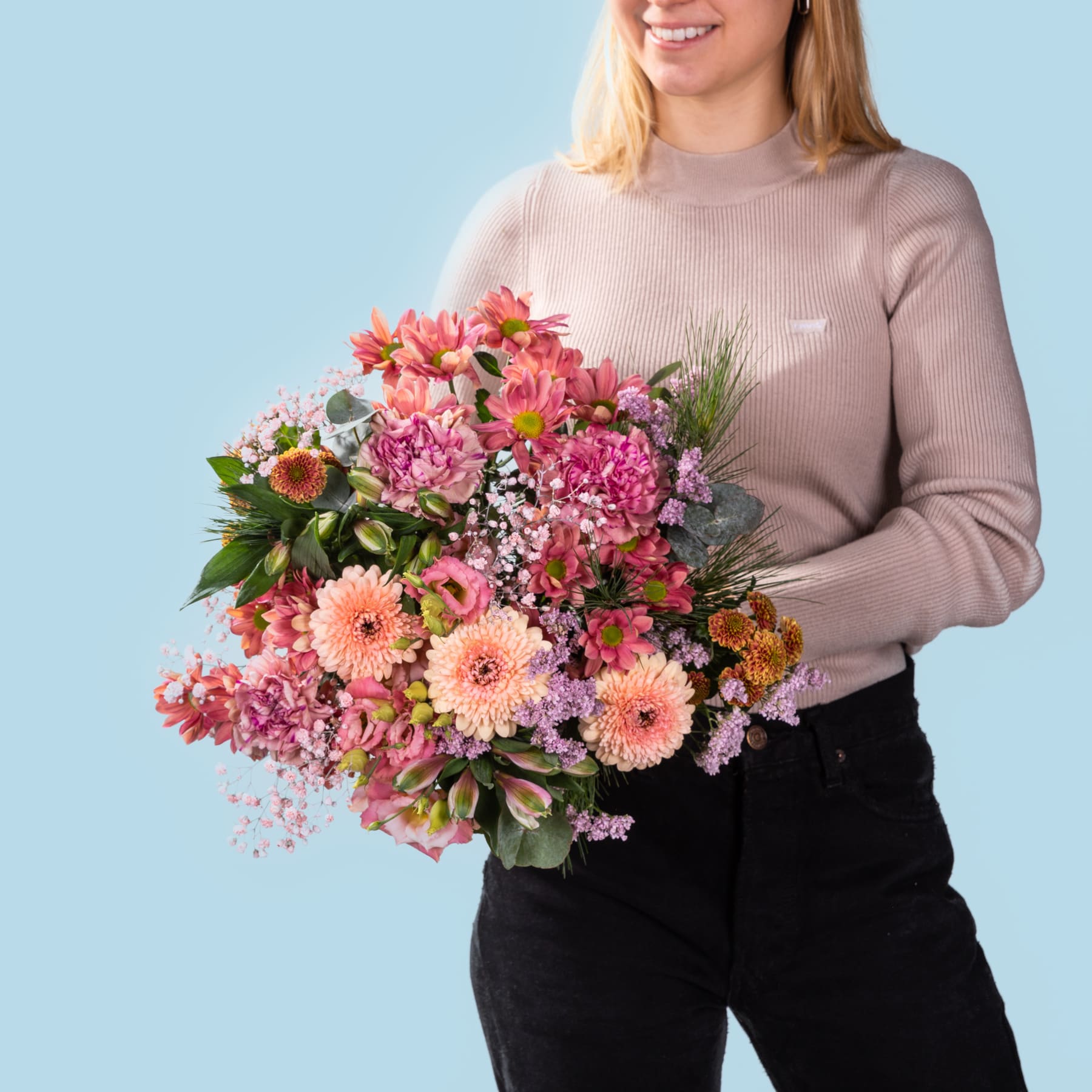 Eine lächelnde Frau hält einen farbenfrohen Strauß rosa und orangefarbener Blumen vor einem schlichten blauen Hintergrund.
