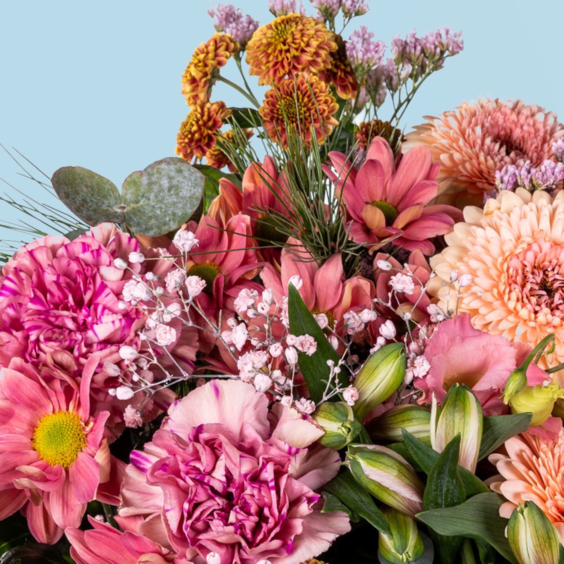 Ein lebendiger Strauß bunter Blumen, darunter rosa Nelken, orangefarbene Chrysanthemen und violette Dahlien, vor einem sanften blauen Hintergrund.