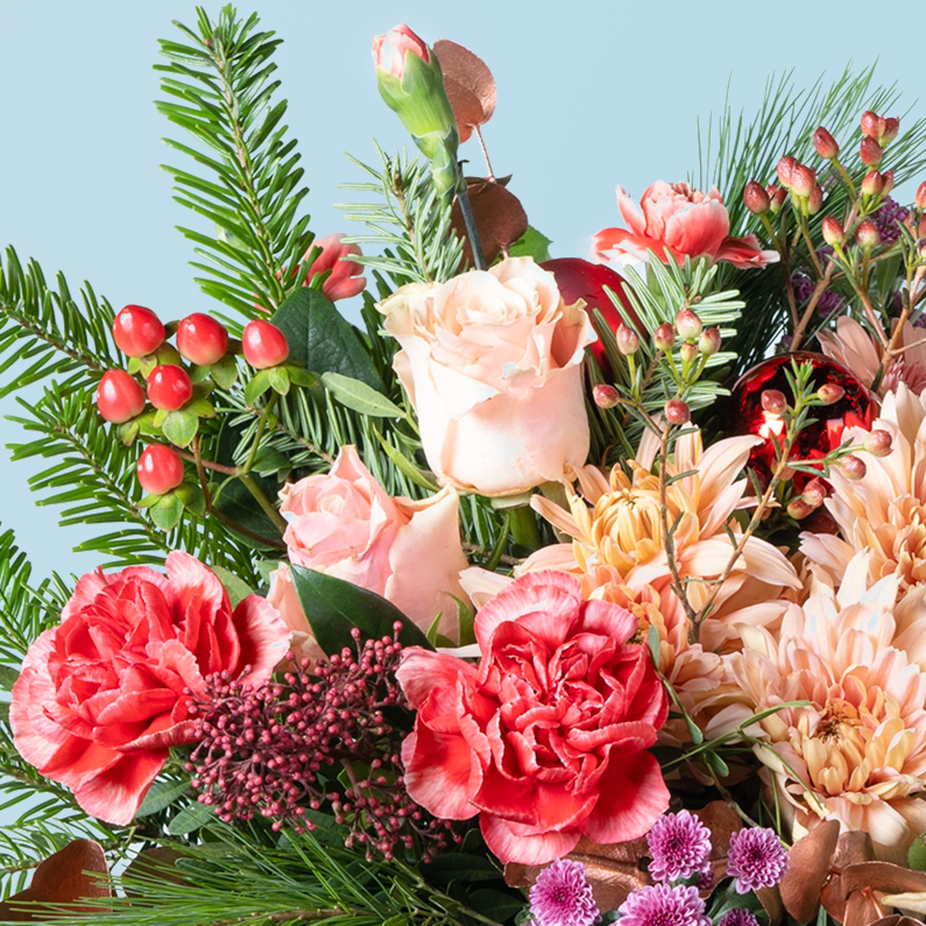 Ein lebendiger Strauß verschiedener Blumen, darunter Rosen, Nelken und Chrysanthemen, umgeben von üppigem Grün und Beeren vor einem sanften blauen Hintergrund.