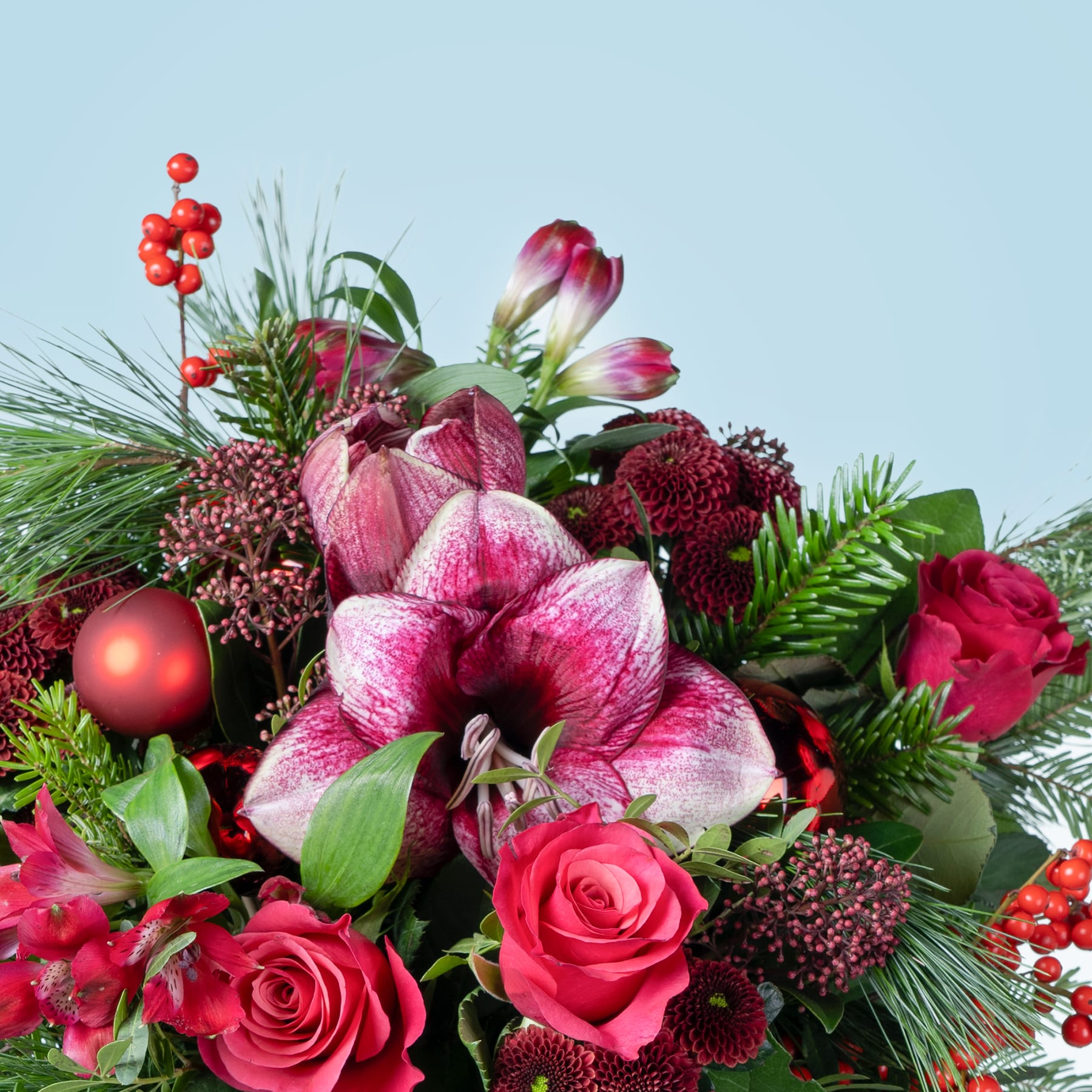 Ein leuchtender Strauß roter und rosa Blumen, darunter Rosen, Lilien und andere Blüten, vor dem Hintergrund eines klaren blauen Himmels.