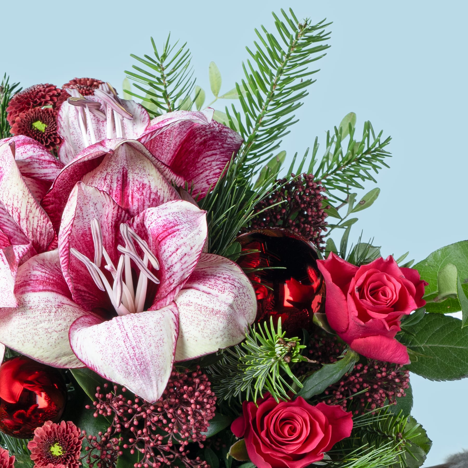 Ein lebendiger Strauß rosa und roter Blumen, darunter Rosen und eine große, auffällige Lilie, umgeben von üppigem grünem Laub vor einem hellblauen Hintergrund.