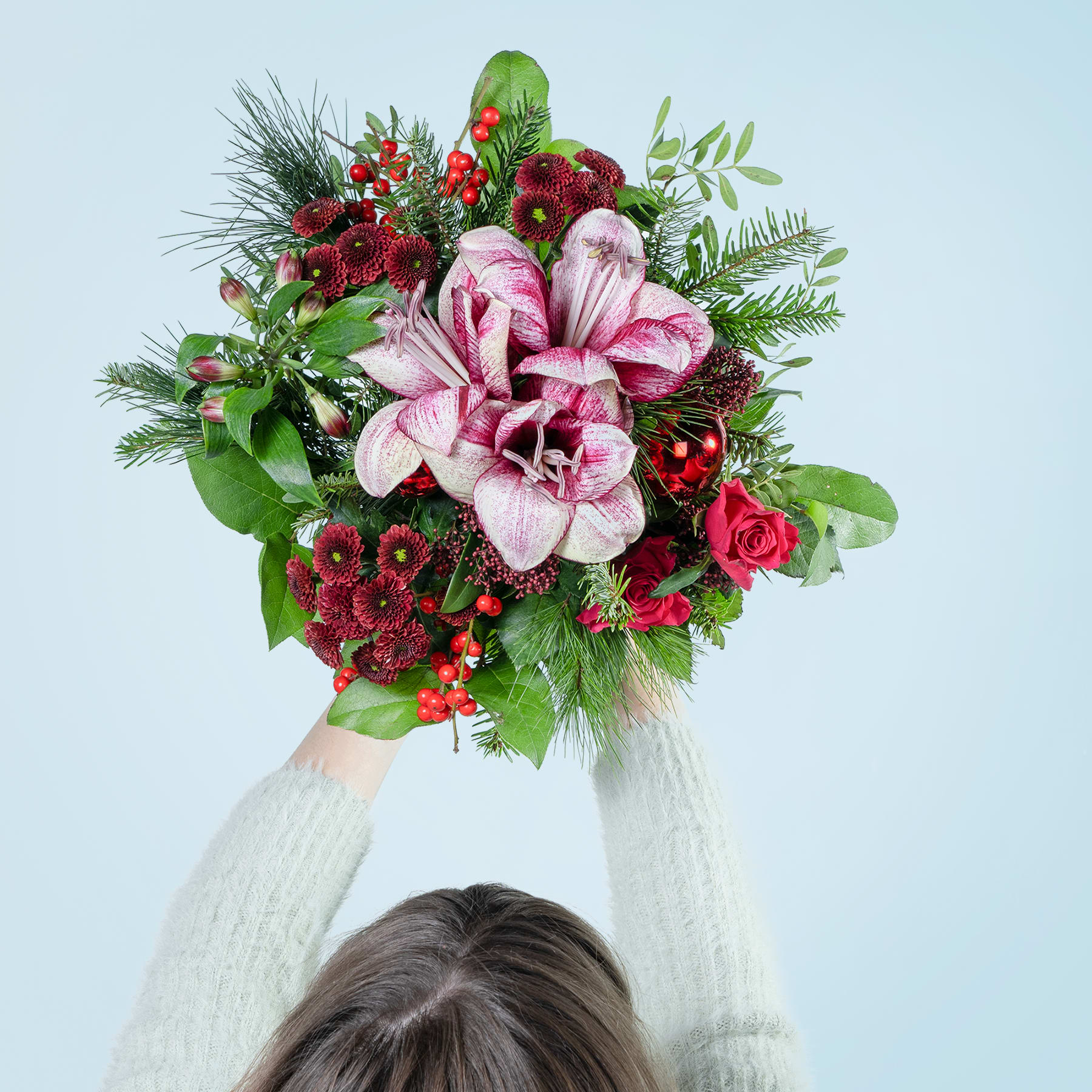 Ein farbenfroher Strauß rosa und roter Blumen, darunter eine große rosa Dahlie, wird vor einem schlichten hellblauen Hintergrund hochgehalten.