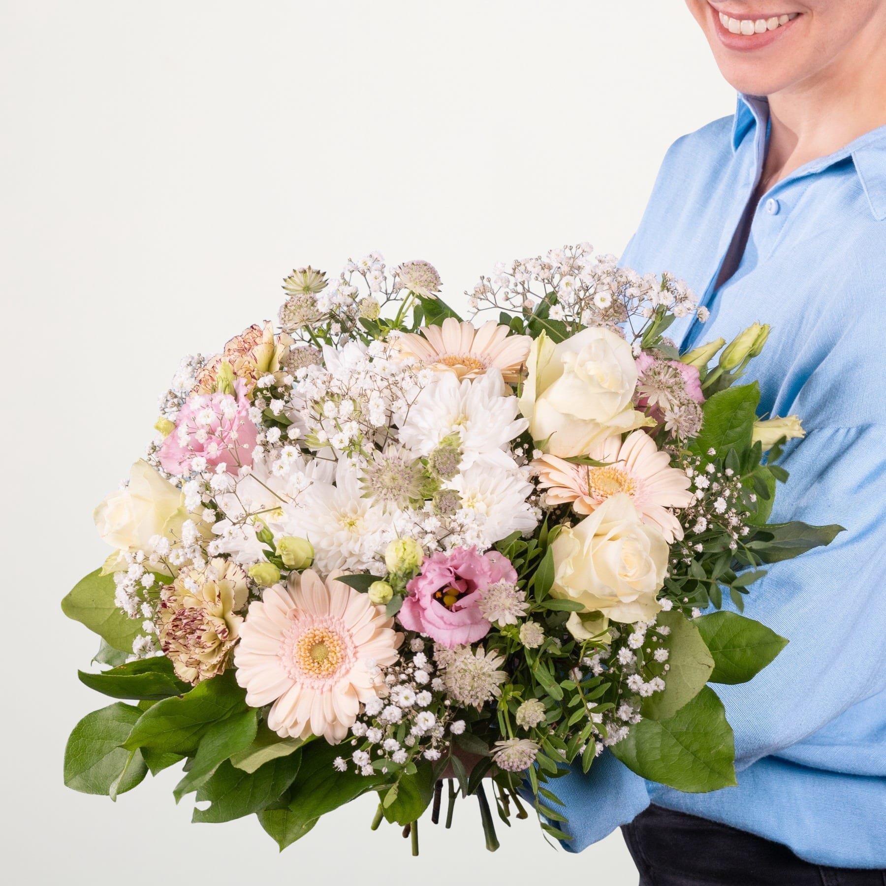 Ein leuchtender Strauß bunter Blumen, darunter Rosen, Gerbera und Schleierkraut, gehalten von einer Person in einem blauen Hemd vor einem schlichten Hintergrund.
