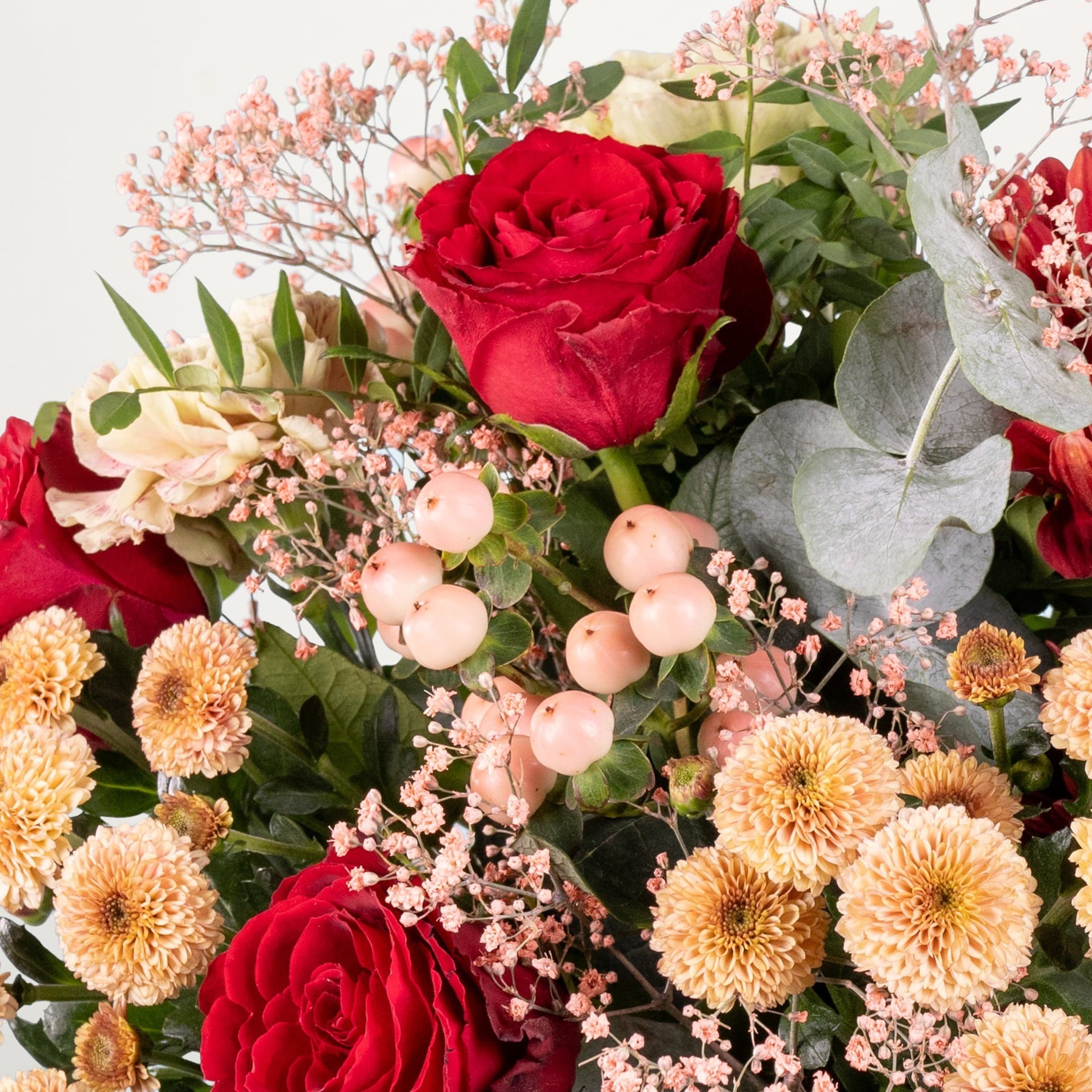 Ein leuchtender Strauß roter Rosen, rosa und gelben Chrysanthemen und anderer üppiger Grünpflanzen füllt den Rahmen und schafft ein optisch beeindruckendes und harmonisches Blumenarrangement.