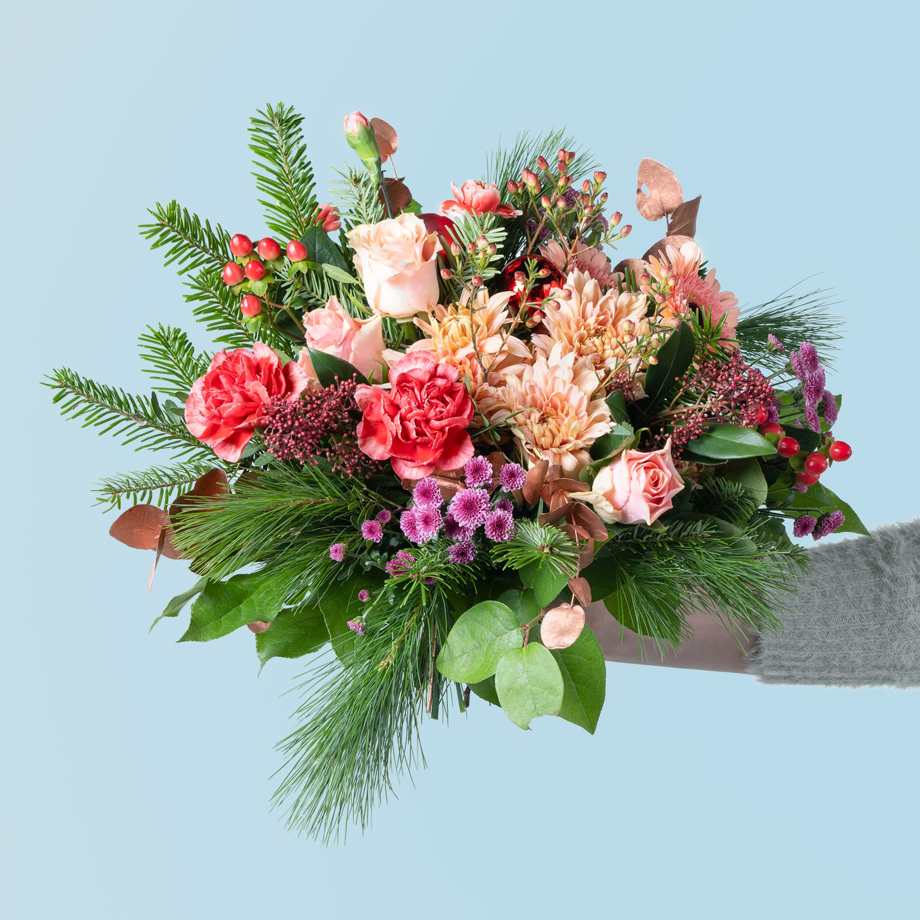 Vor einem hellblauen Hintergrund wird ein farbenfroher Strauß verschiedener Blumen, darunter Rosen, Nelken und Grünpflanzen, präsentiert.