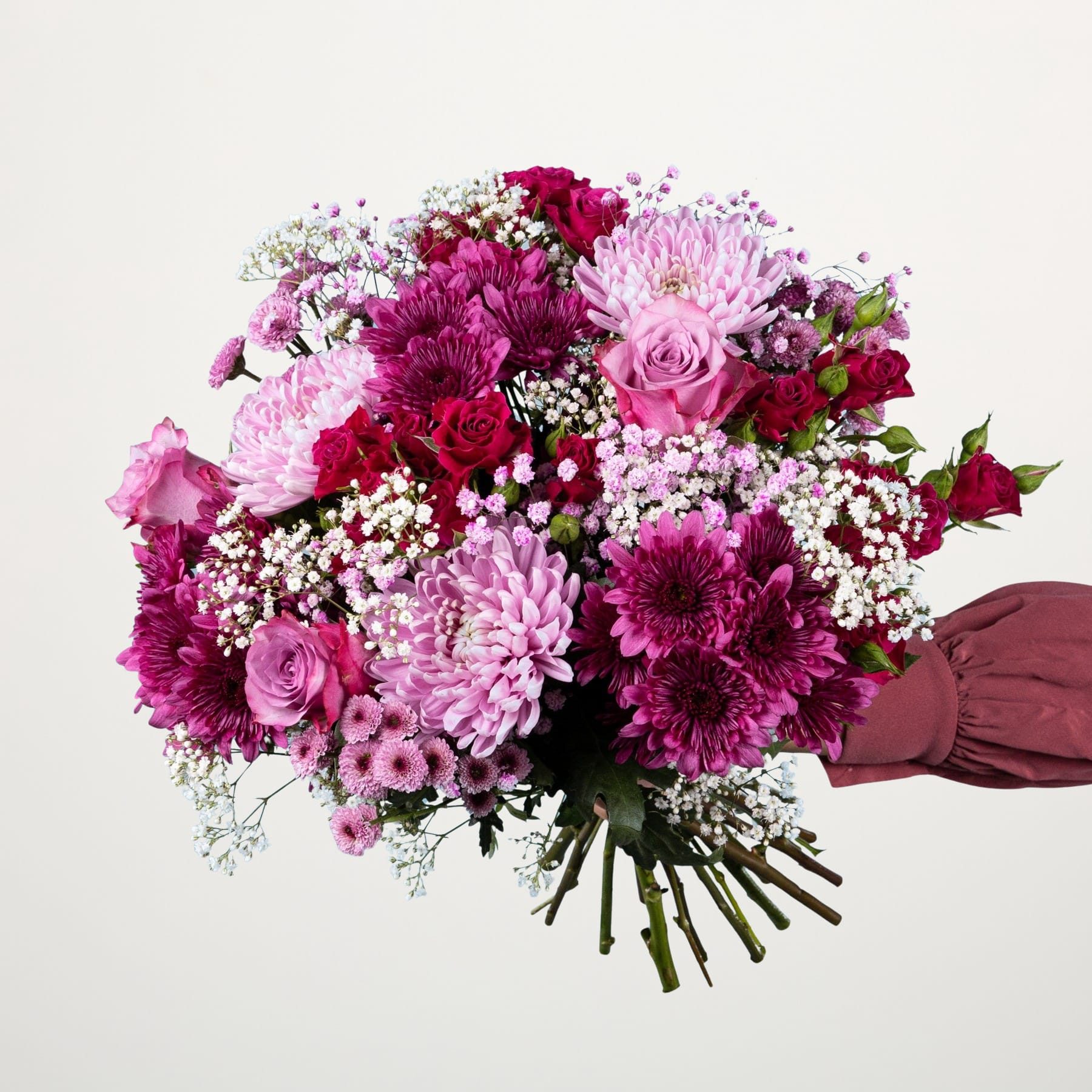 Ein leuchtender Strauß rosa und violetter Blumen, darunter Rosen, Chrysanthemen und Schleierkraut, wird vor einem schlichten weißen Hintergrund in den Händen einer Person gehalten.