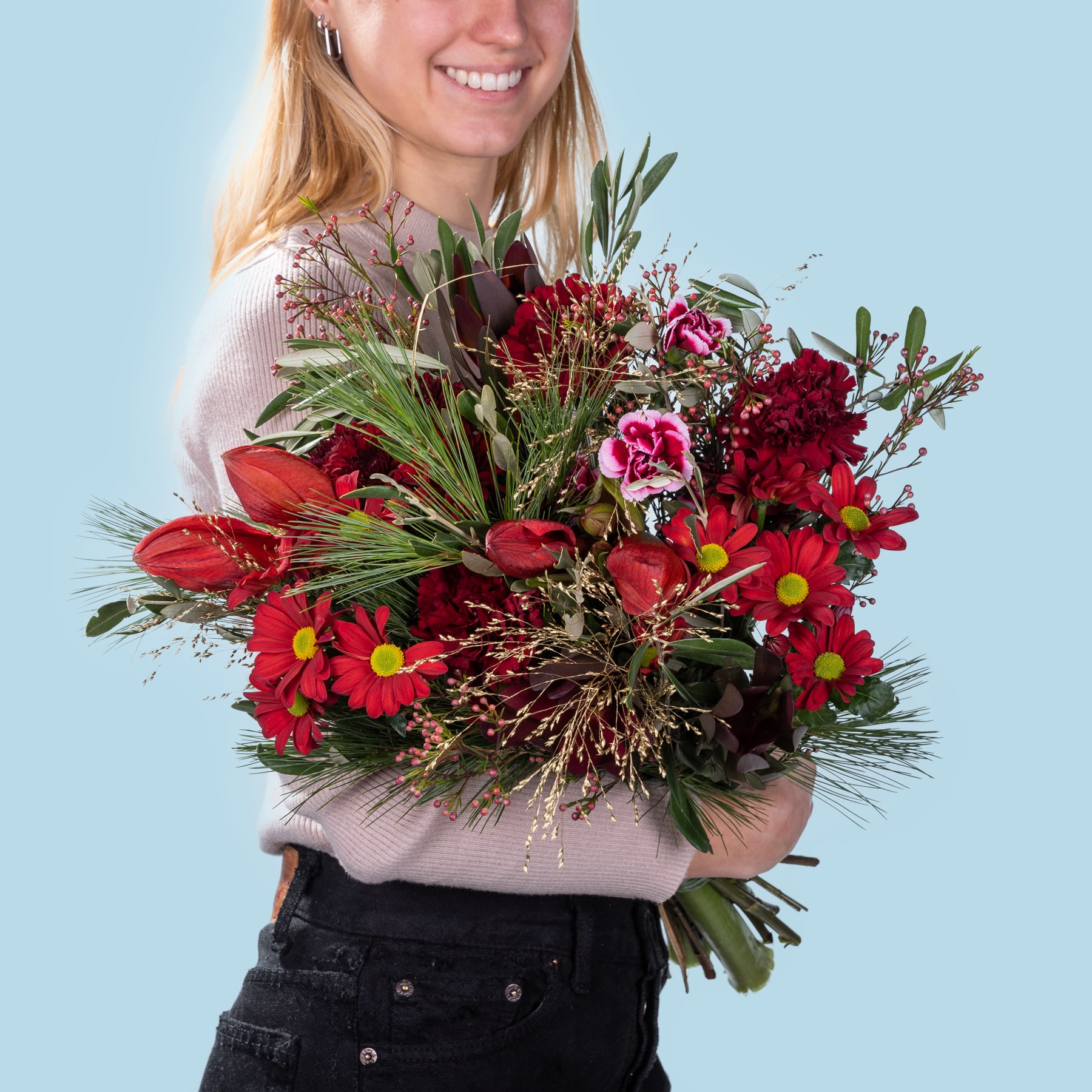 Eine lächelnde junge Frau hält einen farbenfrohen Strauß roter und gelber Blumen vor einem schlichten blauen Hintergrund.
