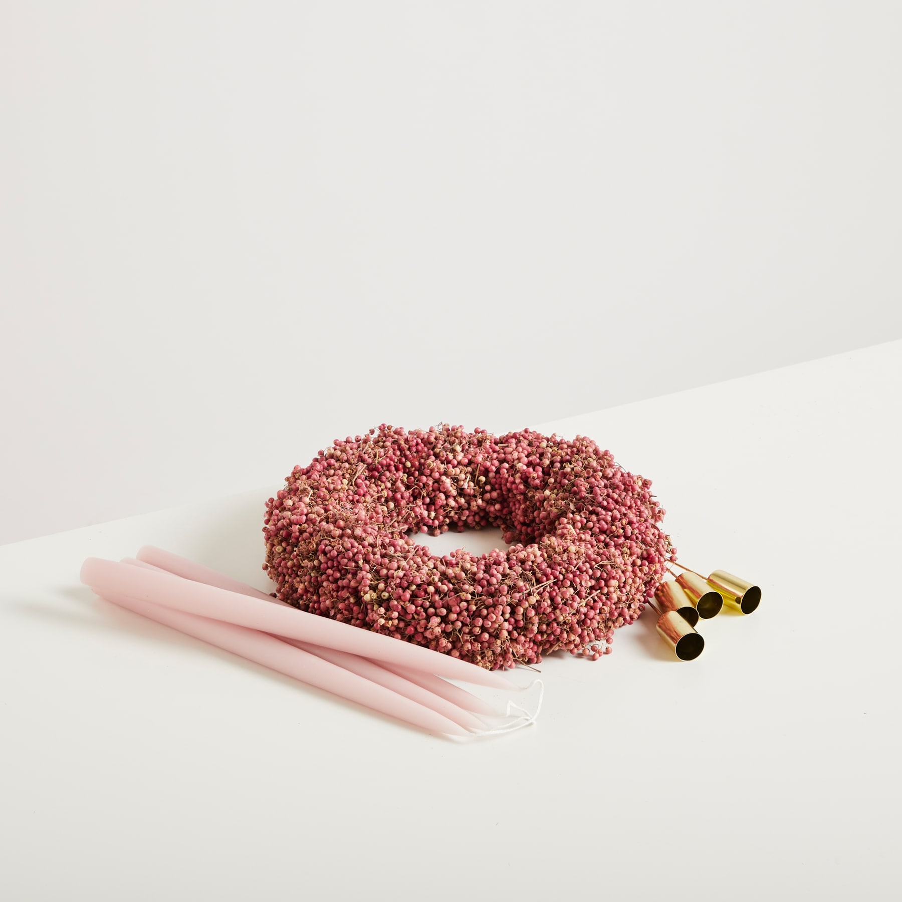 Auf einem schlichten weißen Untergrund liegt ein rosafarbenes, ringförmiges Gebäckstück, das mit roten Streuseln bedeckt ist, und wird von ein paar rosafarbenen Stäbchen begleitet.