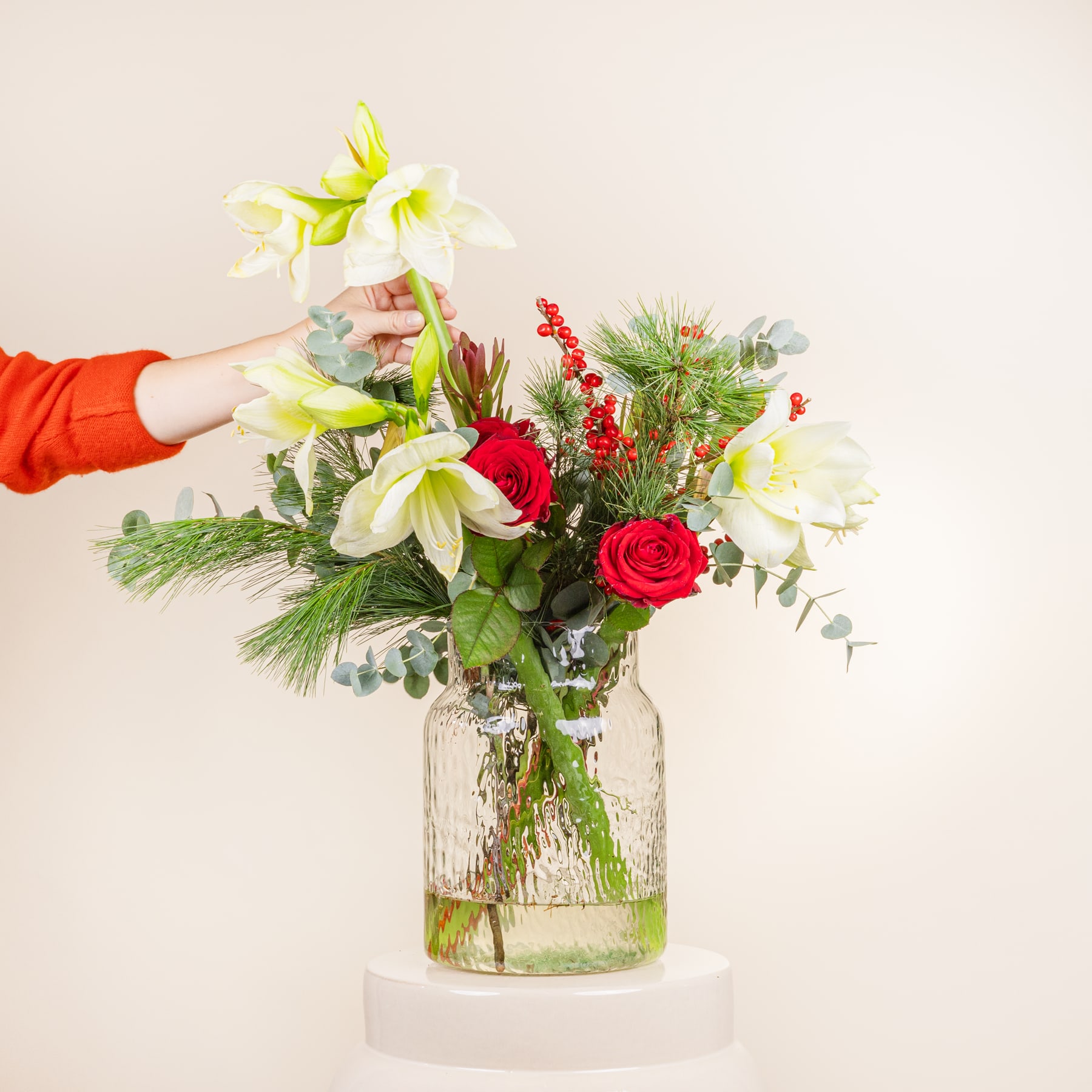 Ein farbenfroher Blumenstrauß mit roten Rosen, weißen Lilien und Grünpflanzen wird in einer Glasvase auf weißem Hintergrund präsentiert.