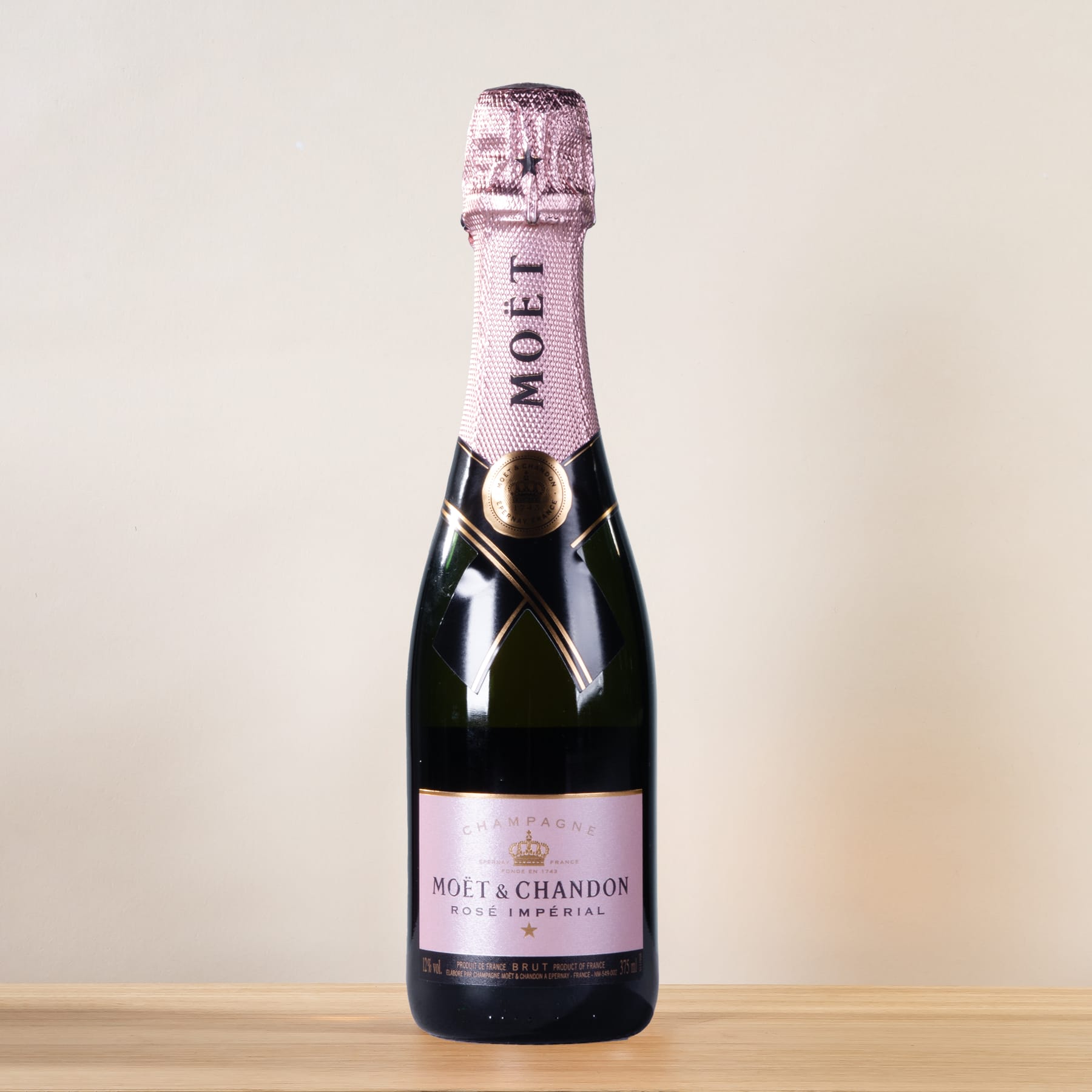 Eine Flasche Champagner von Moët & Chandon steht auf einer Holzoberfläche vor einem schlichten, hellen Hintergrund.