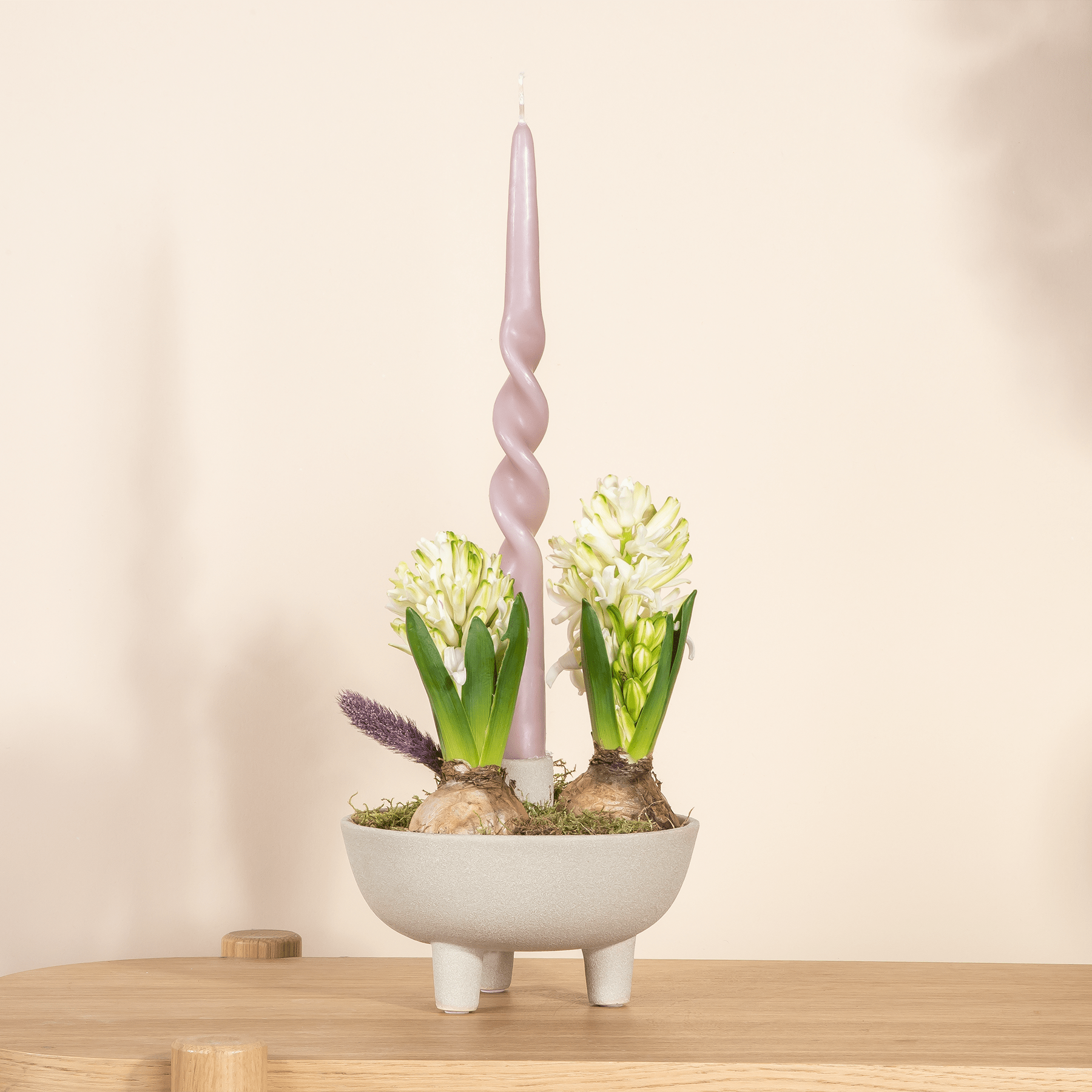 Eine weiße Keramikschale mit zwei blühenden Hyazinthenblüten in leuchtenden Gelb- und Lilatönen vor einem schlichten, hellen Hintergrund.