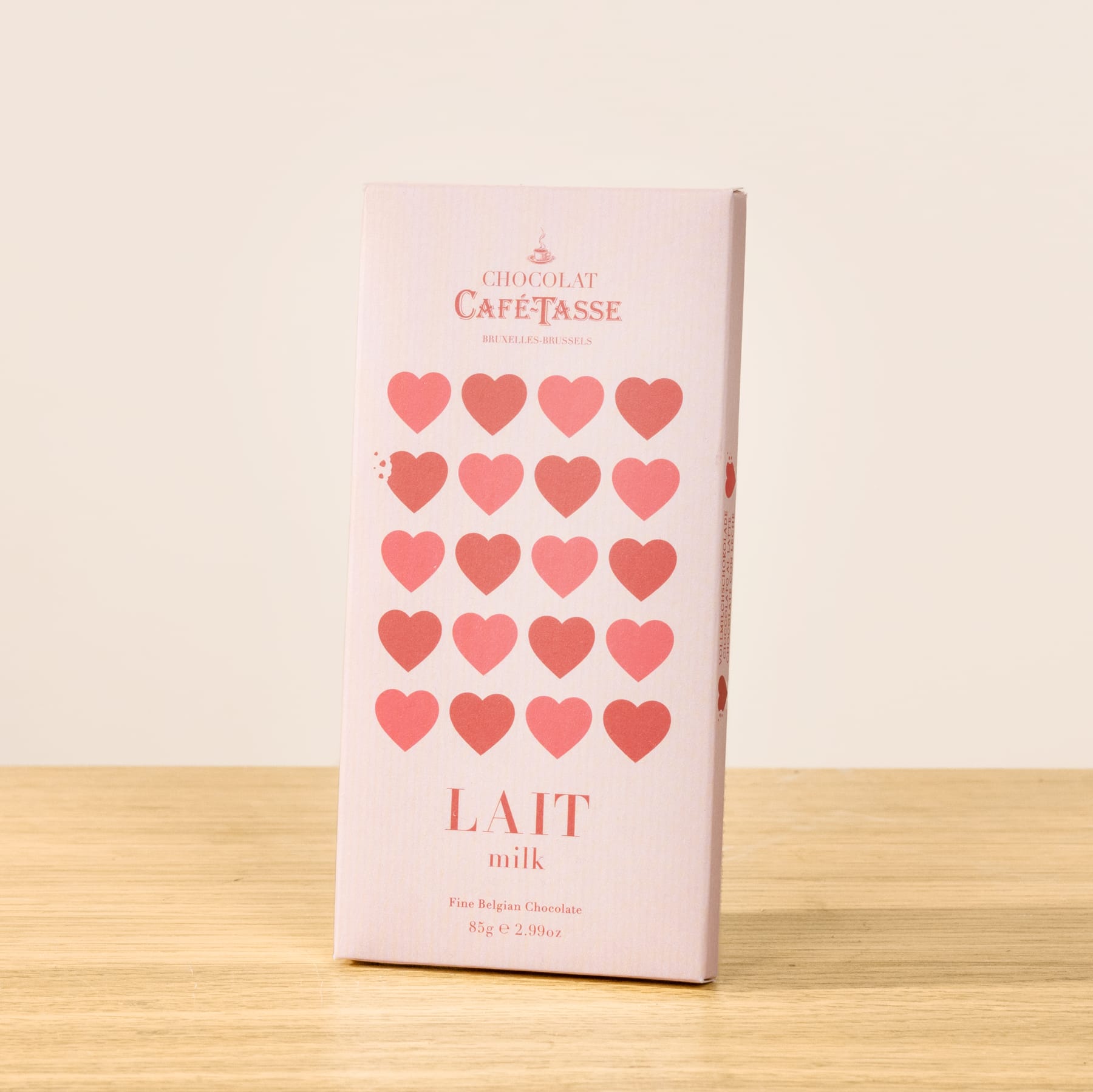 Eine rosafarbene Tafel Schokolade mit einem Muster aus roten Herzen auf der Verpackung, die auf einer Holzoberfläche liegt.