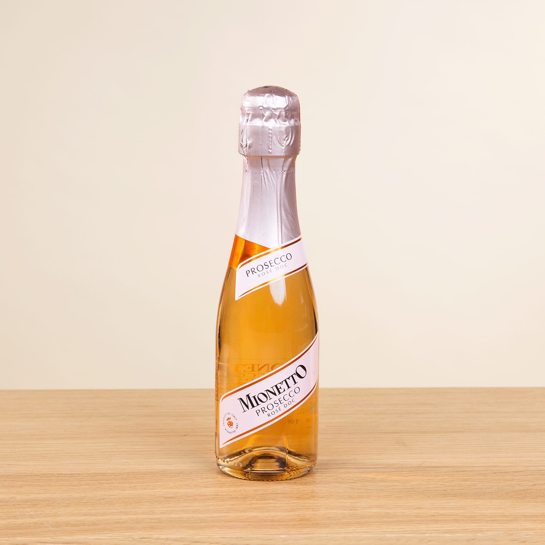 Eine Flasche Miseneta-Sekt steht auf einer Holzoberfläche vor einem schlichten beigen Hintergrund.