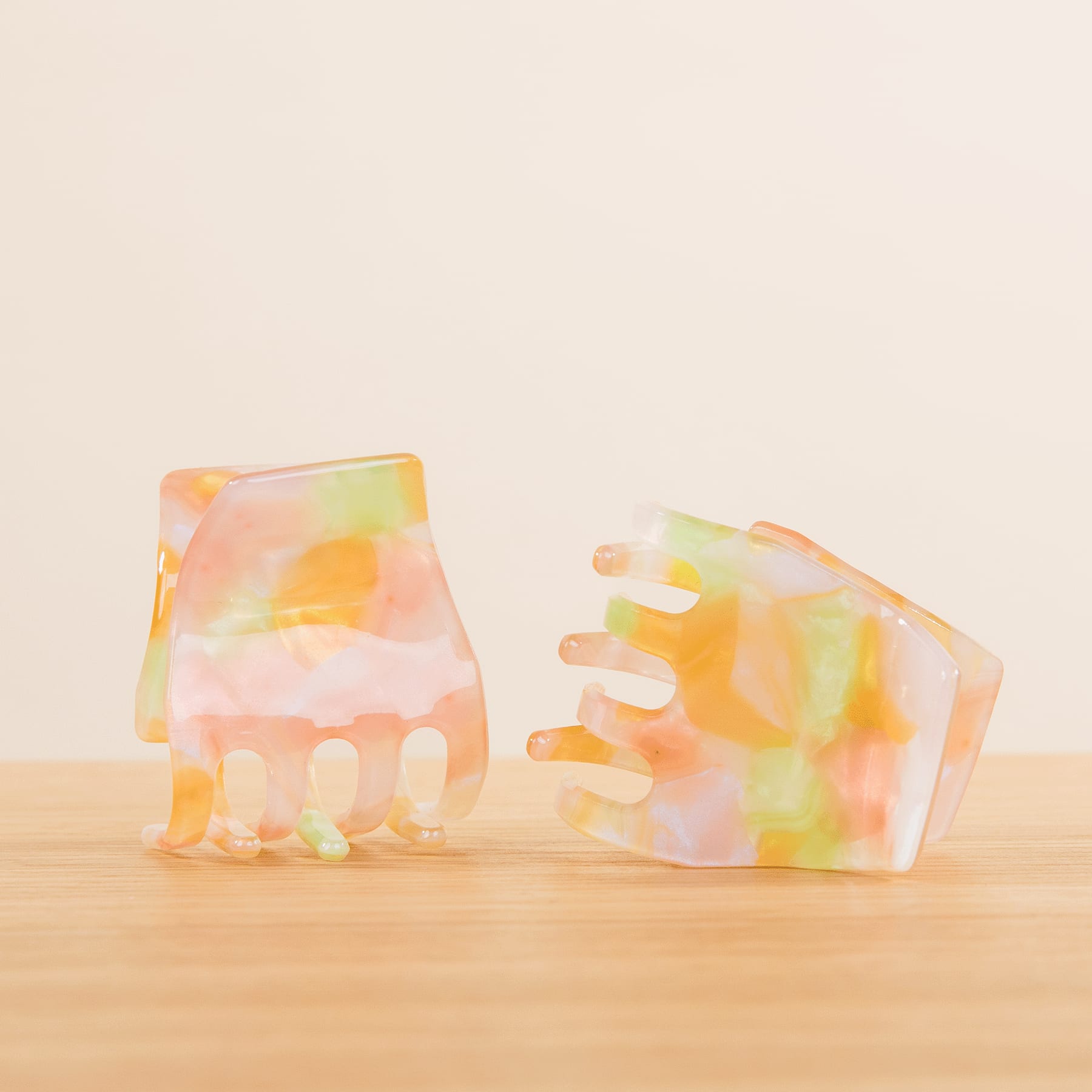 Zwei bunte, durchscheinende handförmige Objekte liegen auf einer Holzoberfläche vor einem schlichten Hintergrund.