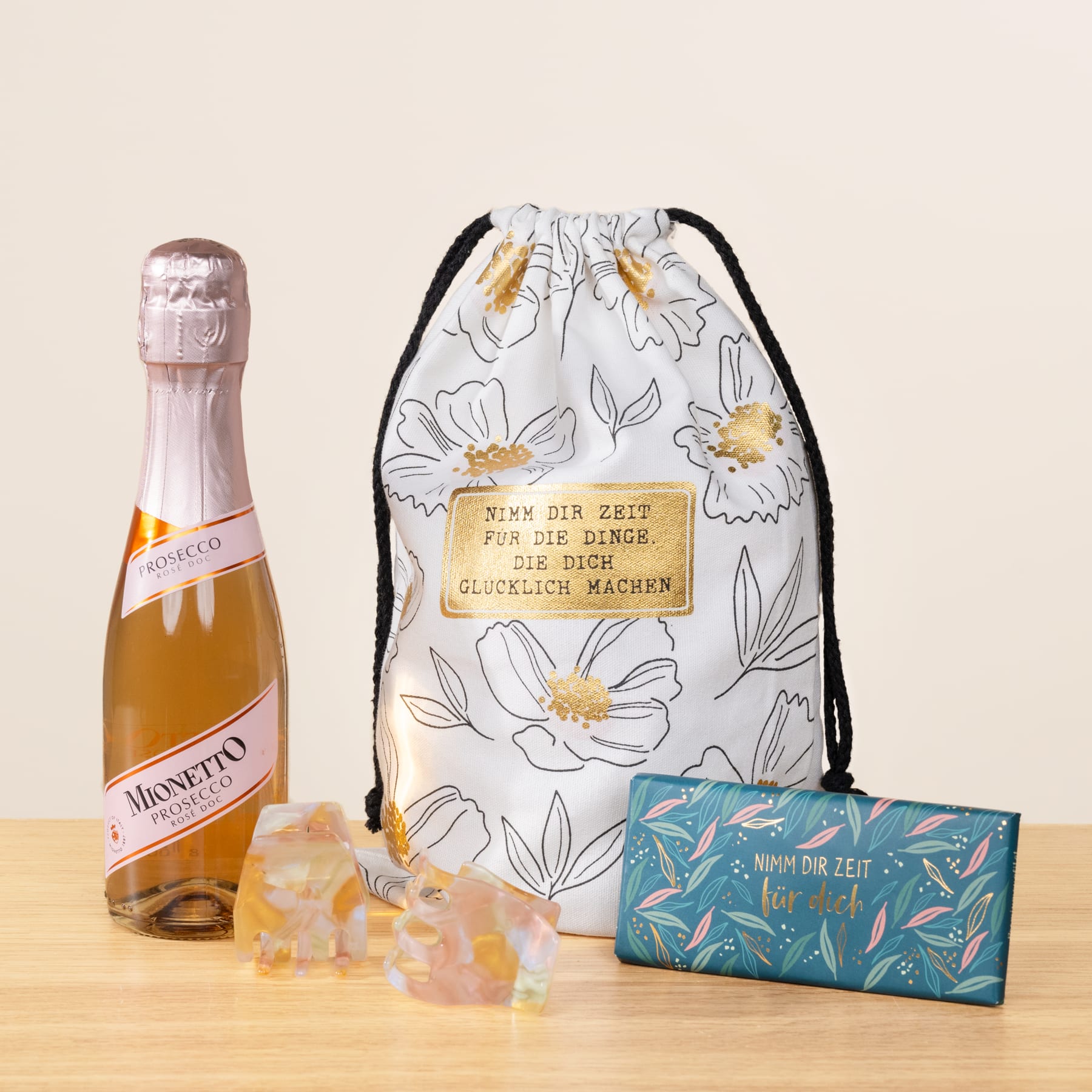 Eine Flasche Moscato-Wein, ein Beutel mit Blumenmuster und eine Schachtel Badesalz sind auf einer Holzoberfläche vor einem hellen Hintergrund angeordnet.