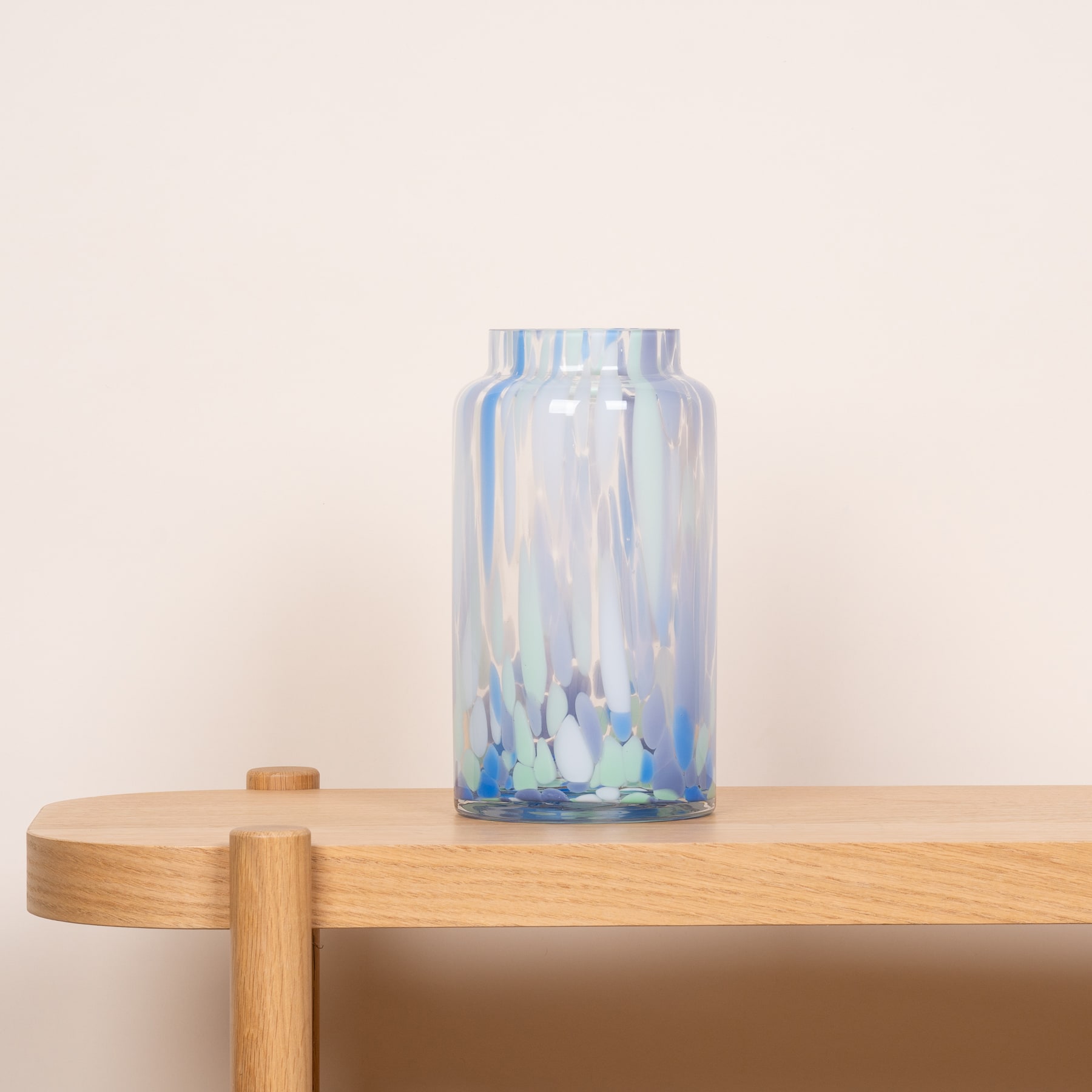 Eine klare Glasvase mit einem blau-weiß schillernden Muster steht auf einem Holztisch vor einem schlichten beigen Hintergrund.