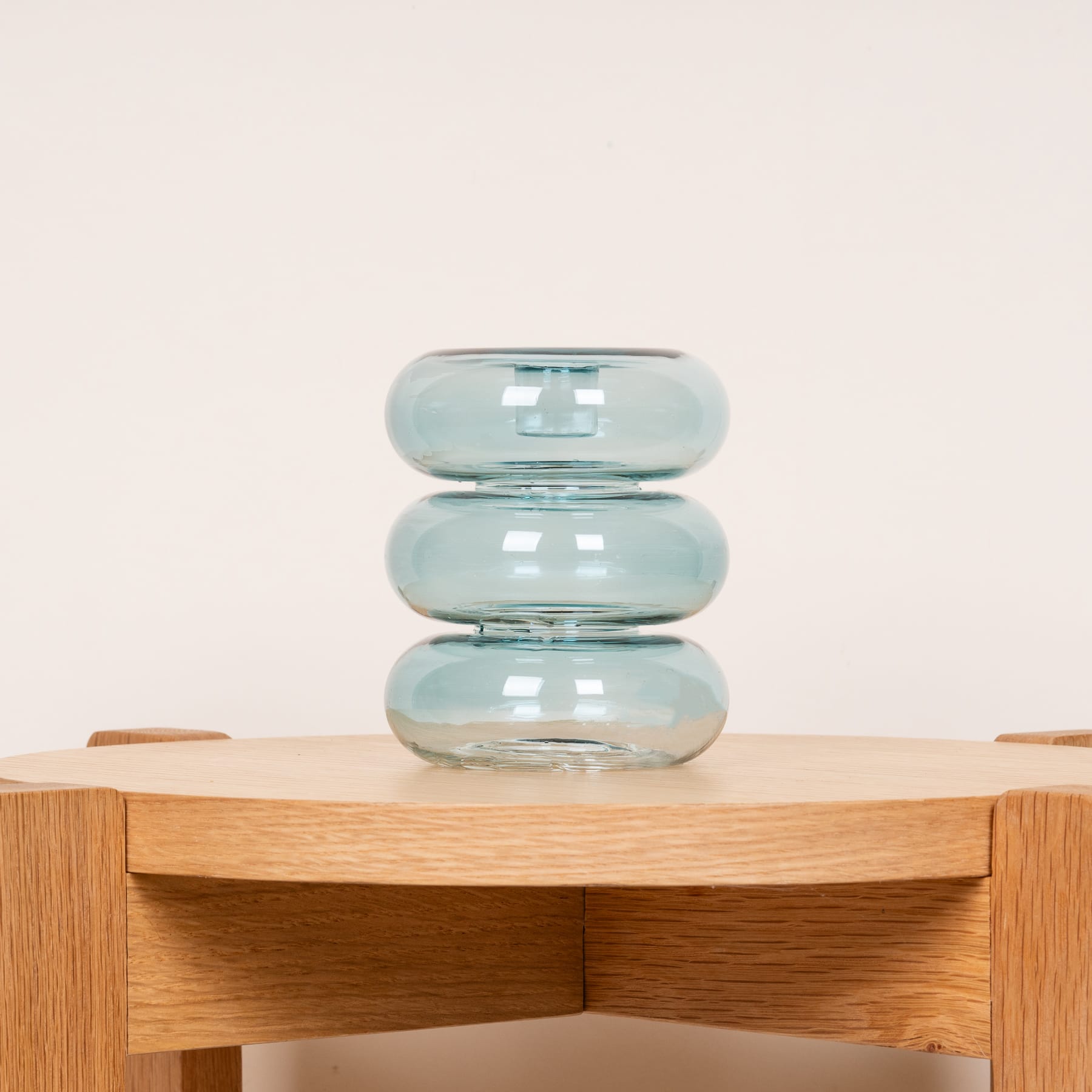 Ein Stapel aus drei Glasvasen in unterschiedlichen Blautönen steht auf einem Holztisch oder Regal vor einem schlichten, hellen Hintergrund.