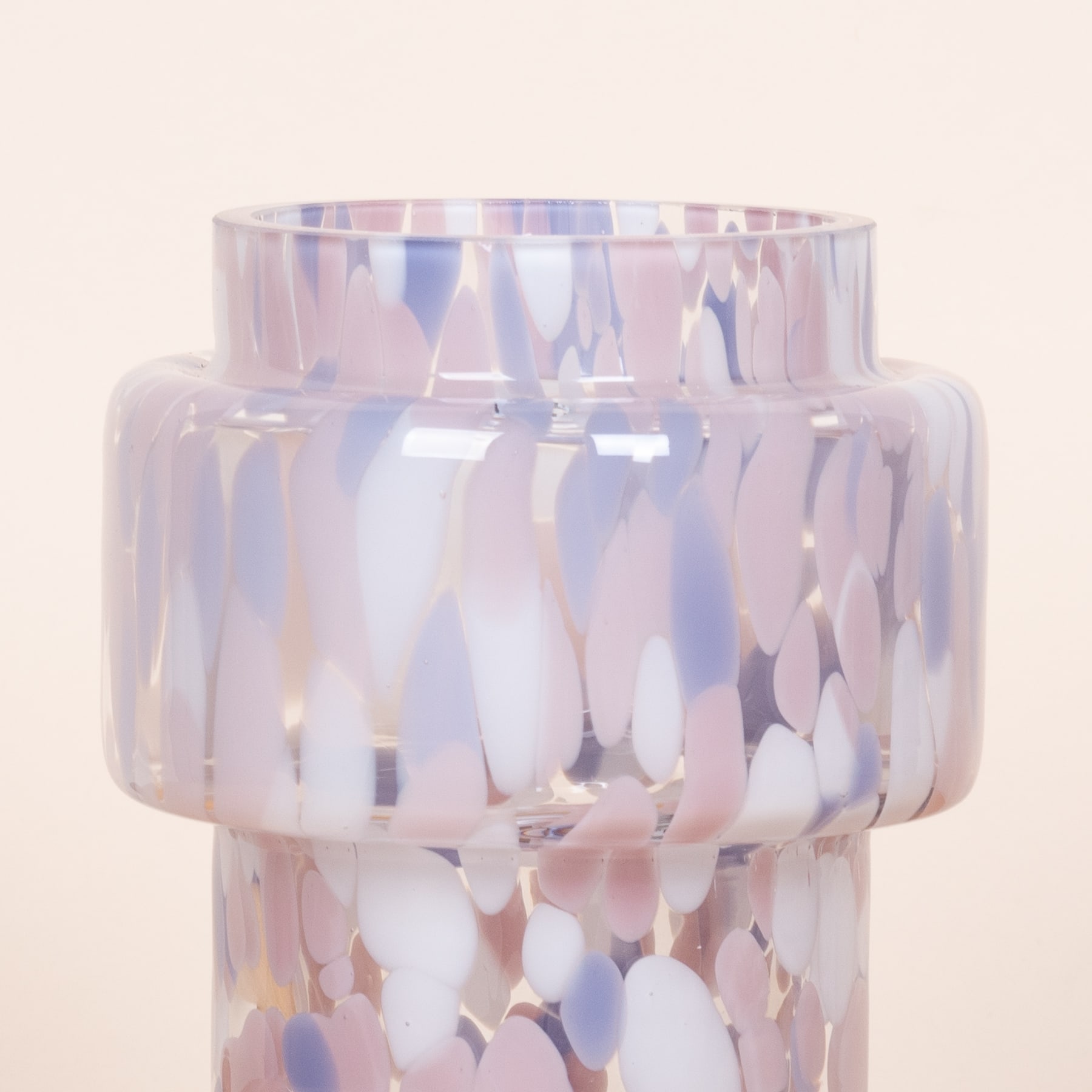 Eine Glasvase oder ein Glasbehälter mit einer strukturierten, schillernden Oberfläche in Rosa-, Lila- und Blautönen vor einem schlichten, hellen Hintergrund.