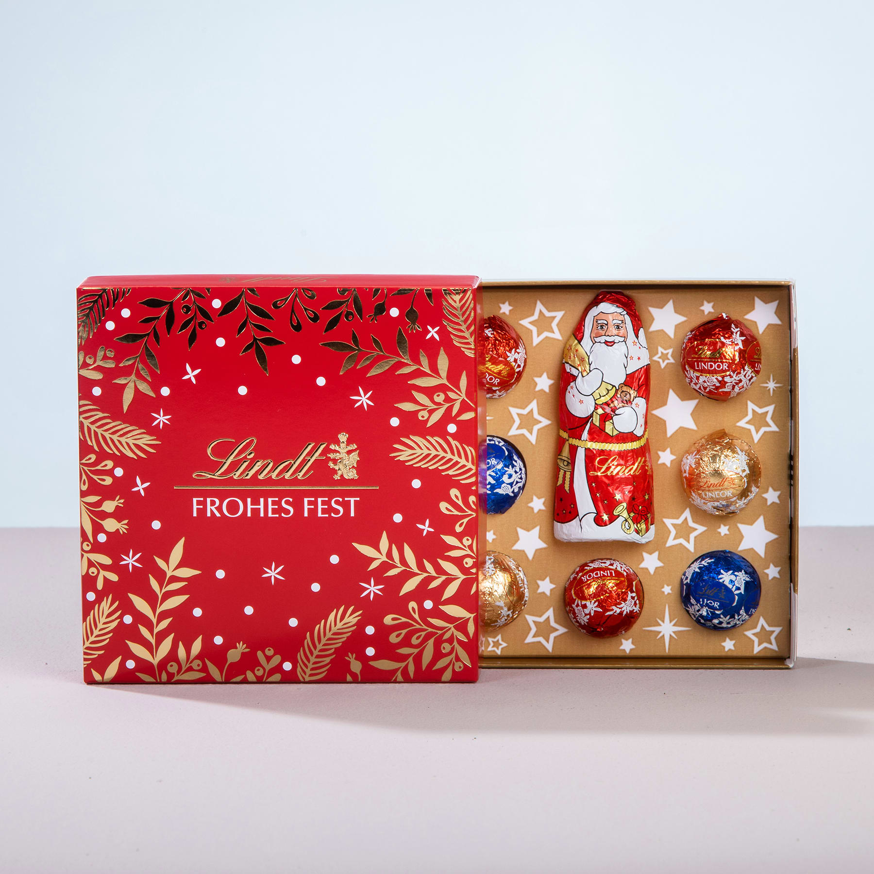 Eine rot-goldene Weihnachtsgeschenkbox mit einer Weihnachtsmannfigur und verschiedenen Ornamenten vor einem schlichten Hintergrund.