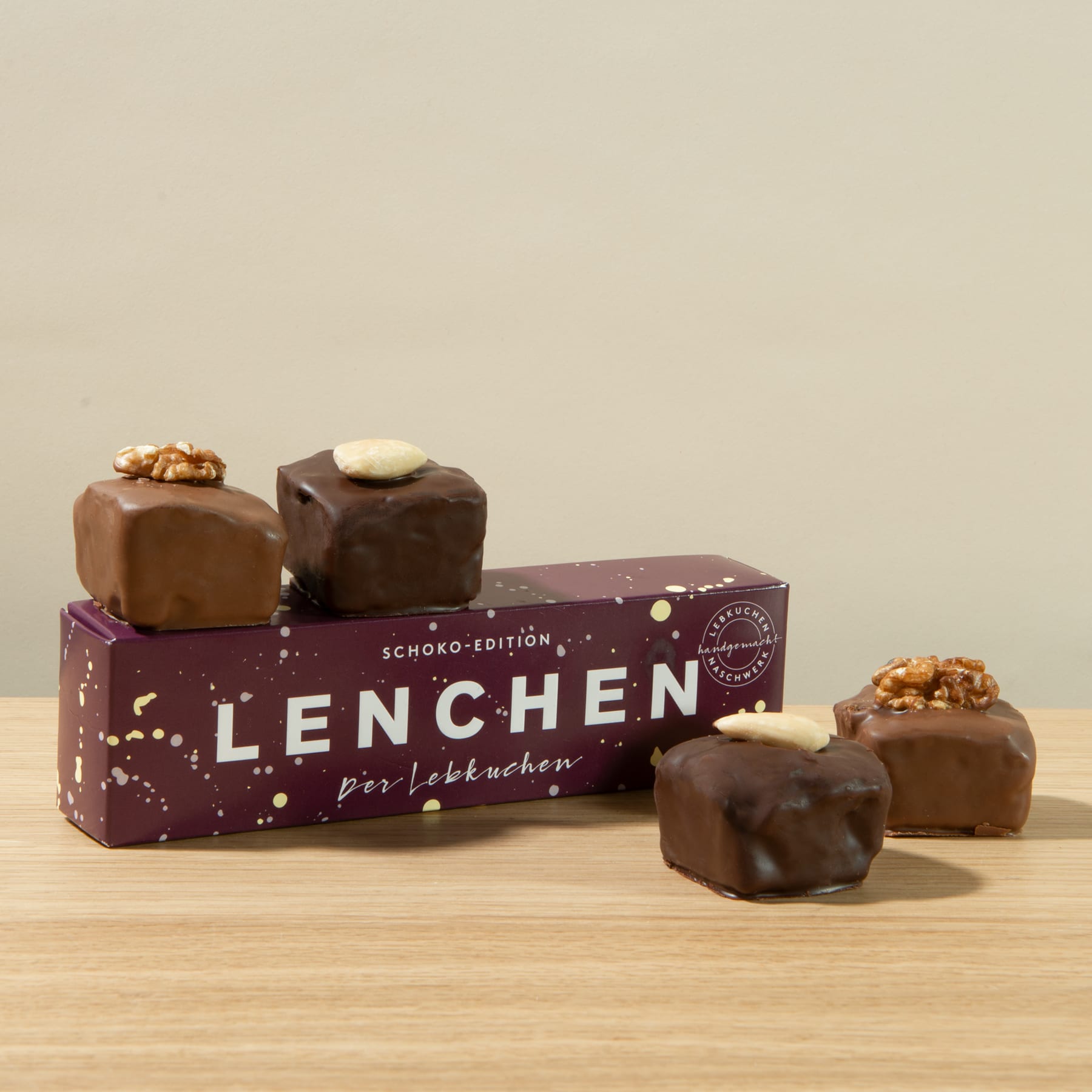 Das Bild zeigt eine Pralinenschachtel namens „Lenchen“ mit mehreren schokoladenüberzogenen Pralinen im Vordergrund, die auf einer Holzoberfläche ruhen.