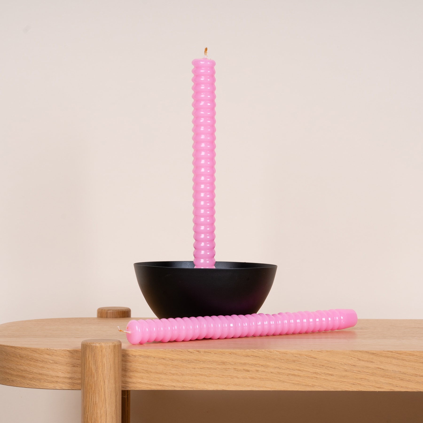 Eine rosa Kerze steht aufrecht in einer schwarzen Schale und ruht auf einem Holztisch oder einer Holzoberfläche.
