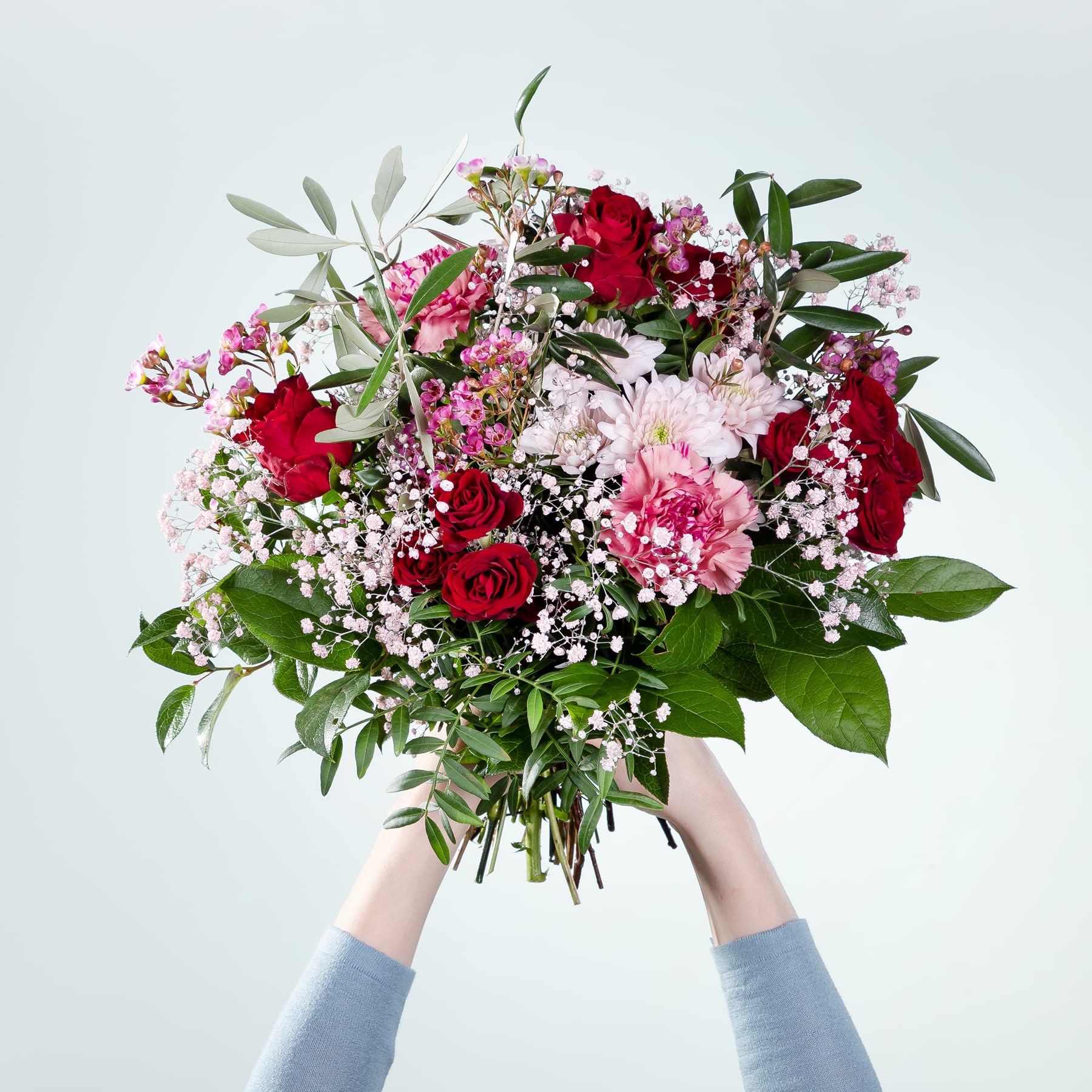 Ein leuchtender Strauß aus roten Rosen, rosa Nelken und weißen Gänseblümchen vor einem schlichten weißen Hintergrund.