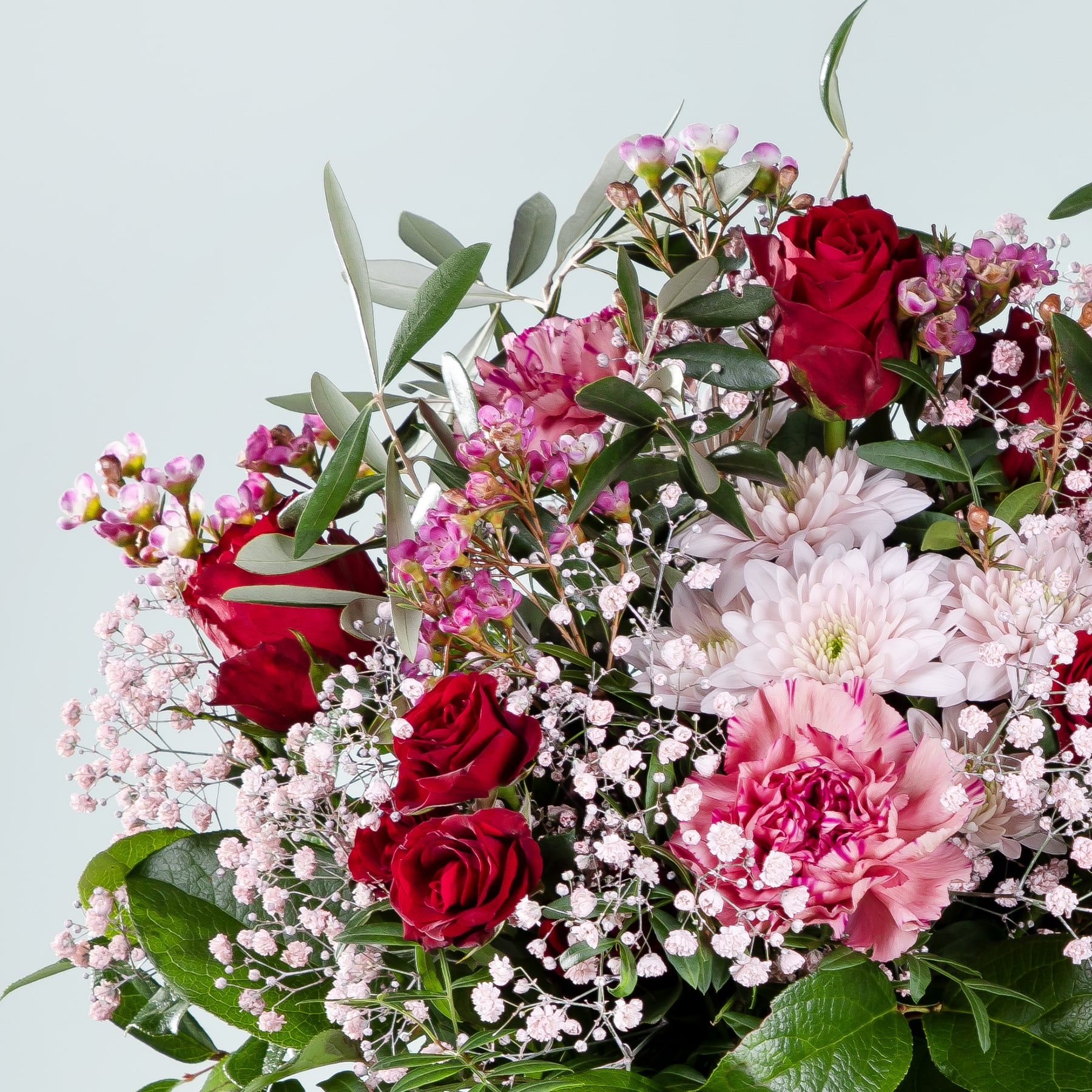 Ein lebendiger Strauß aus roten Rosen, rosa Nelken und weißen Schleierkrautblüten vor hellem Hintergrund.