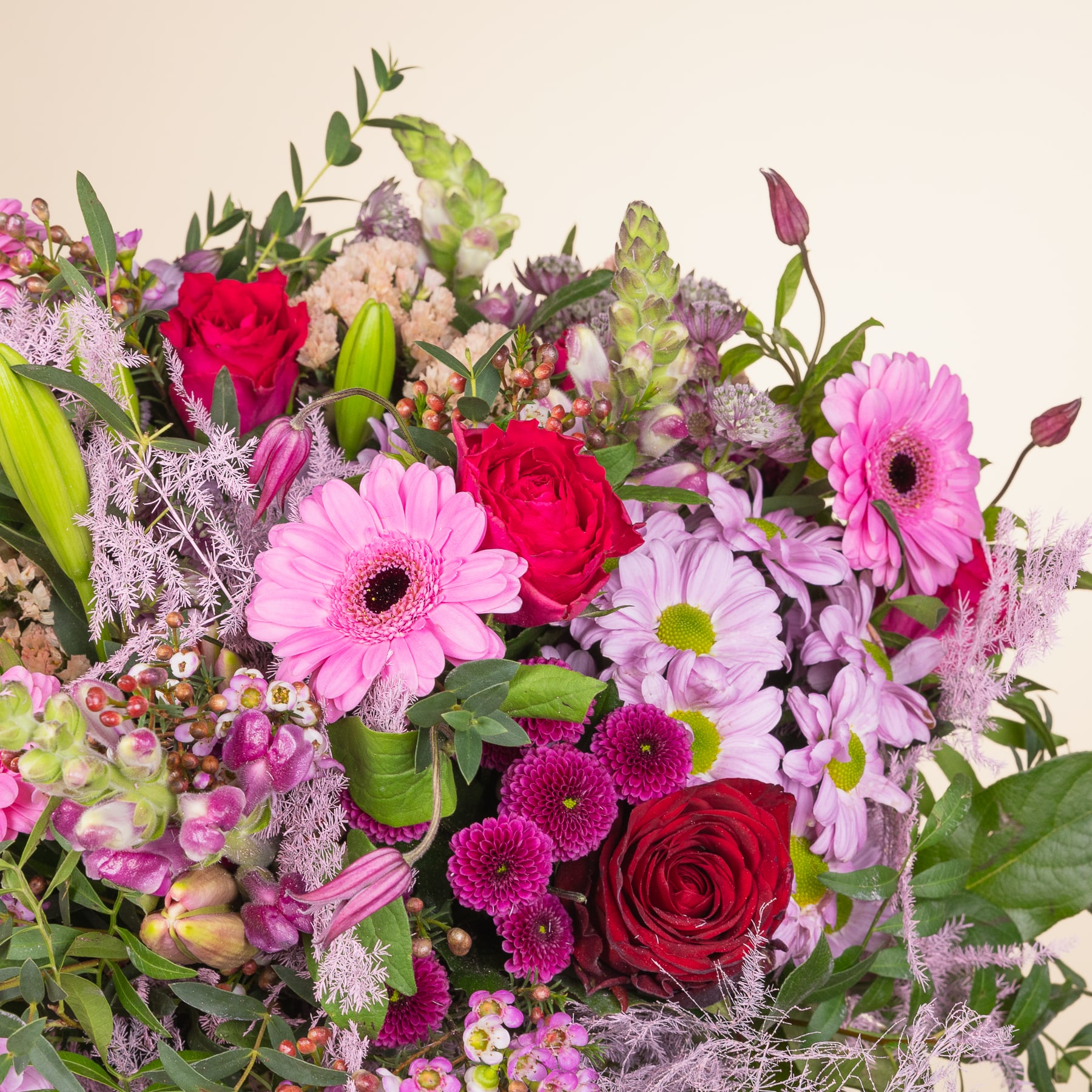 Ein lebendiger Strauß verschiedener bunter Blumen, darunter rote Rosen, rosa Gerbera und lila Chrysanthemen, vor einem hellen Hintergrund.