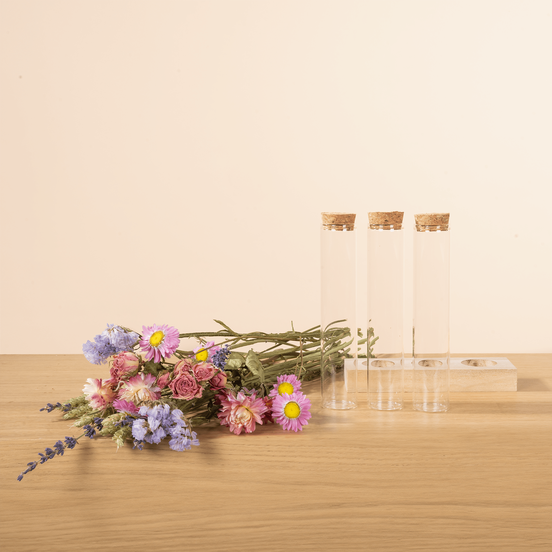 Ein Strauß bunter Blumen, darunter rosa Pfingstrosen, violette Schwertlilien und gelbe Gänseblümchen, steht neben drei Glasgefäßen mit Korkdeckeln auf einem Holztisch.