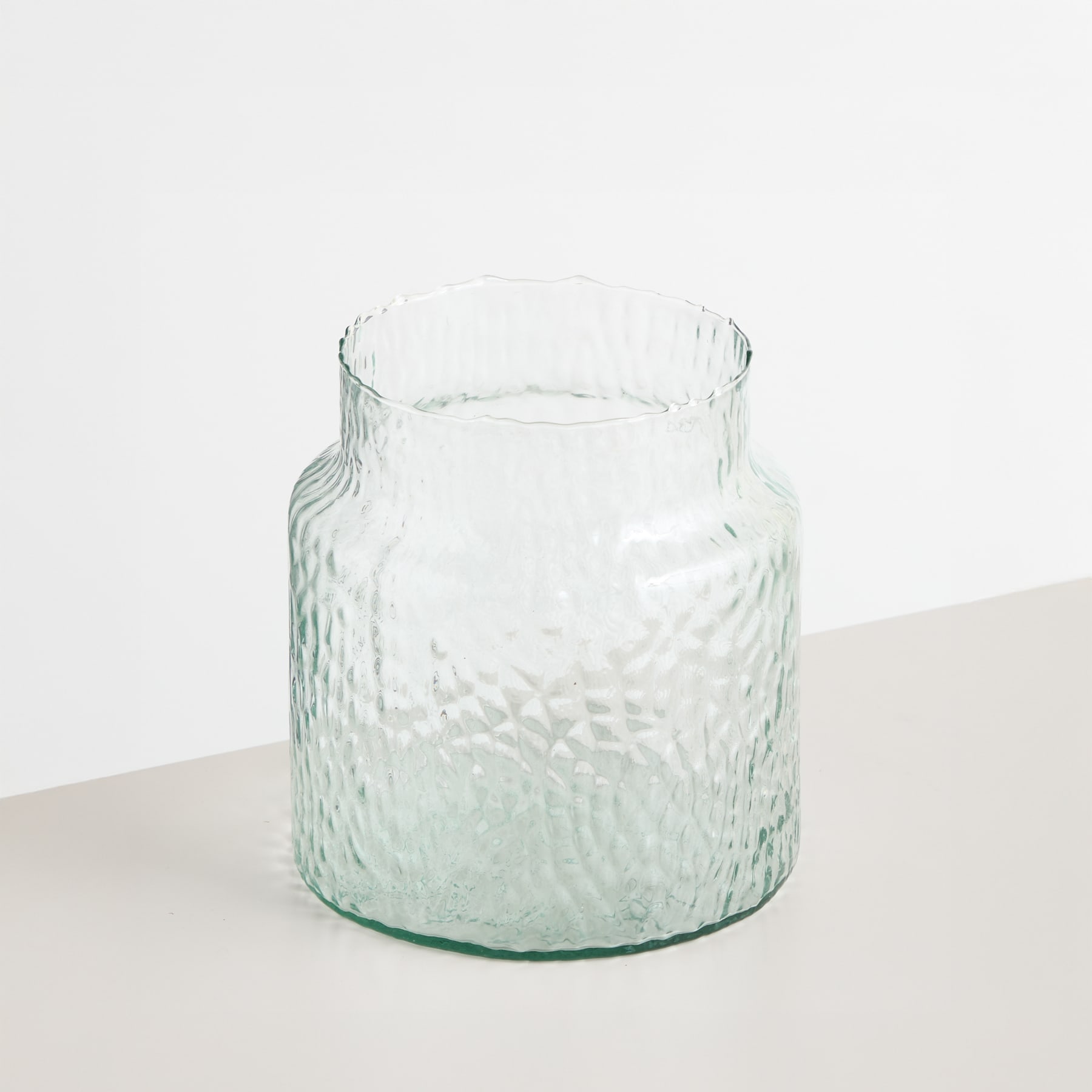 Ein leuchtender Strauß rosa und gelber Tulpen in einer Glasvase vor einem schlichten, hellen Hintergrund.