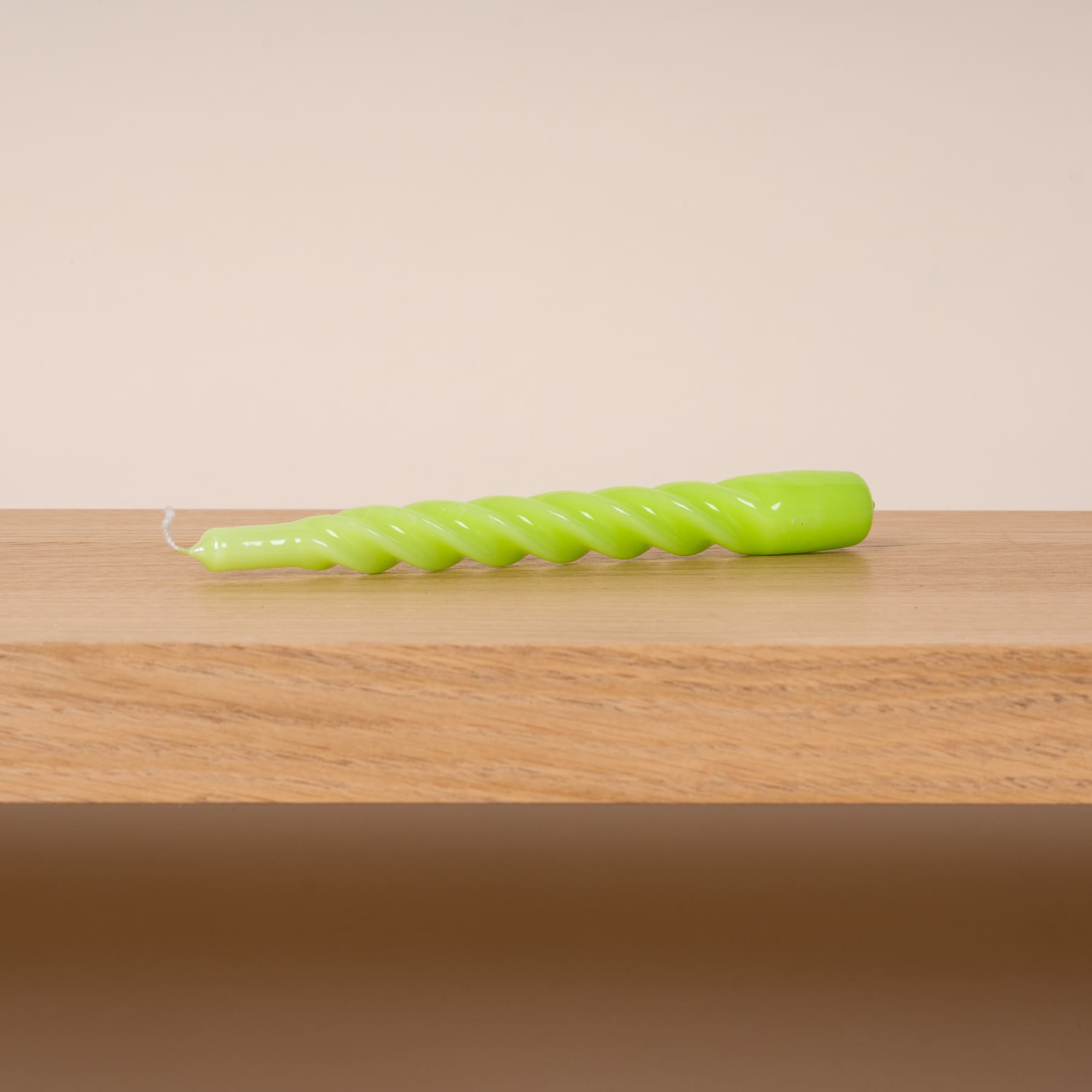 Ein leuchtend grünes, spiralförmiges Gemüse oder Obst liegt auf einer Holzoberfläche vor einem schlichten, hellen Hintergrund.