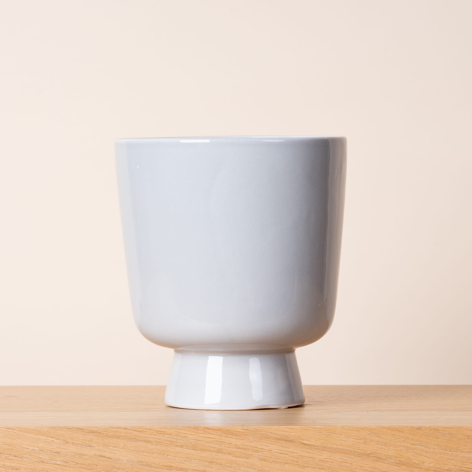 Eine weiße Keramikvase oder -tasse mit Säulenfuß steht auf einer Holzoberfläche vor einem hellen Hintergrund.