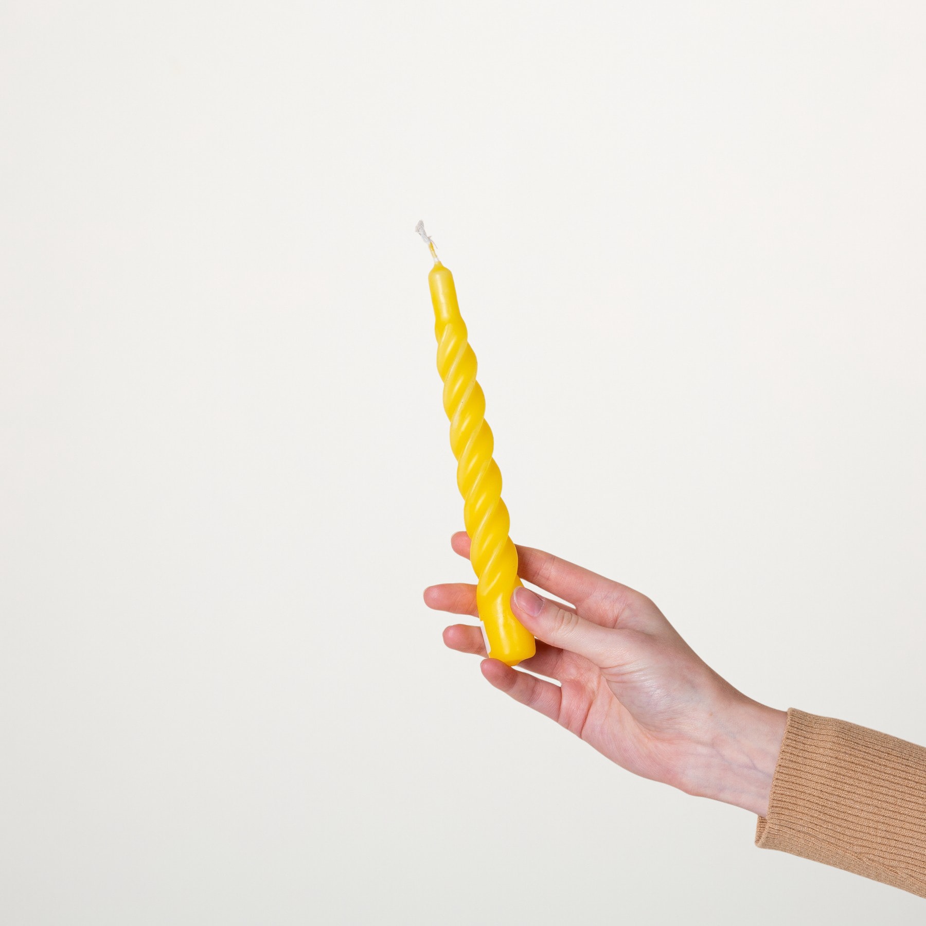 Eine Hand, die eine leuchtend gelbe Spiralkerze vor einem schlichten weißen Hintergrund hält.