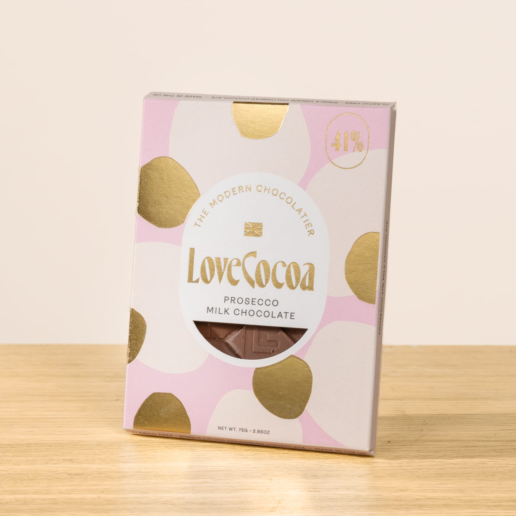 Eine rosa-goldfarbene Schachtel mit Love Cocoa Prosecco-Milchschokolade steht auf einer Holzoberfläche.