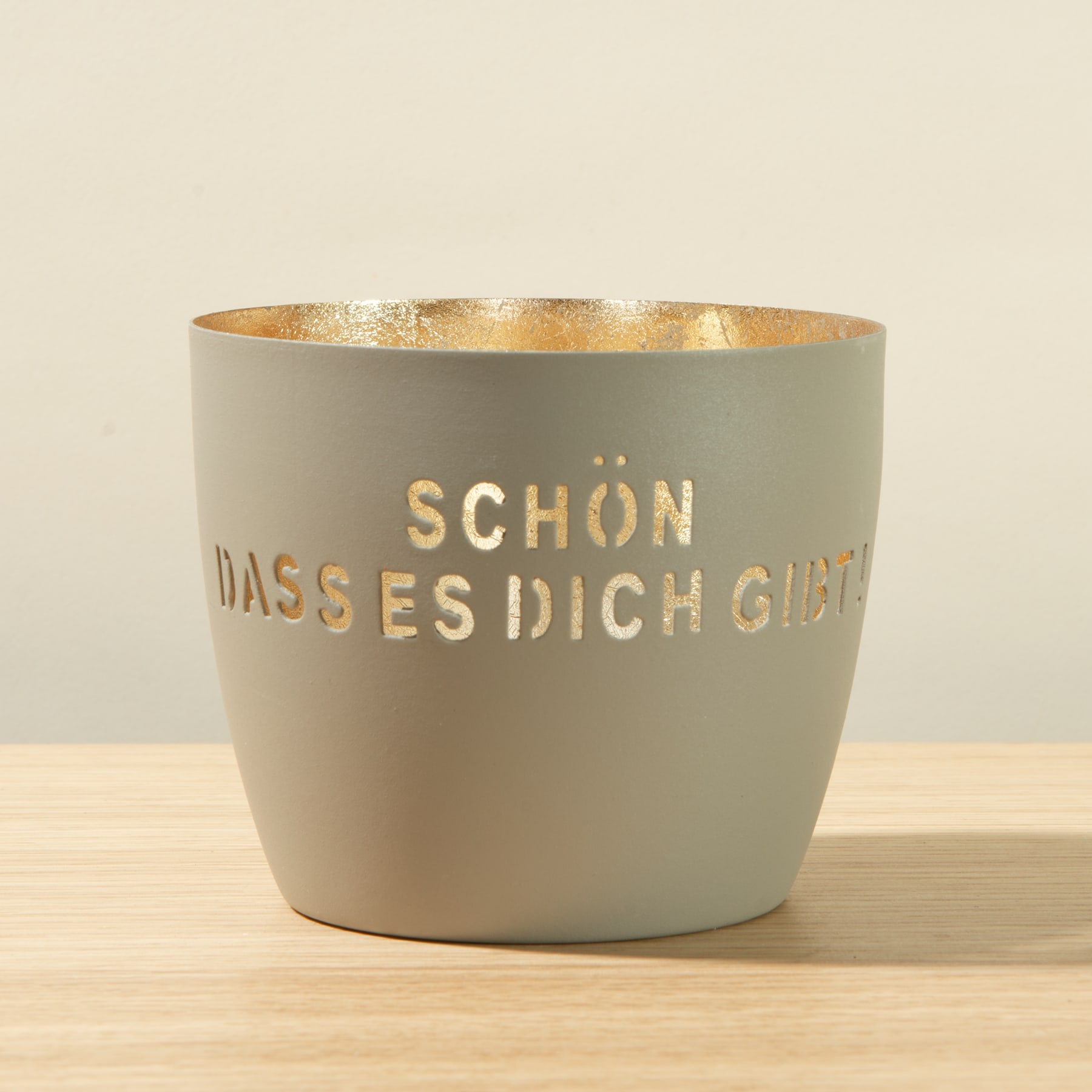 Ein grauer Keramiktopf mit dem Aufdruck „Schön, dass es dich gibt“ steht auf einer Holzoberfläche.