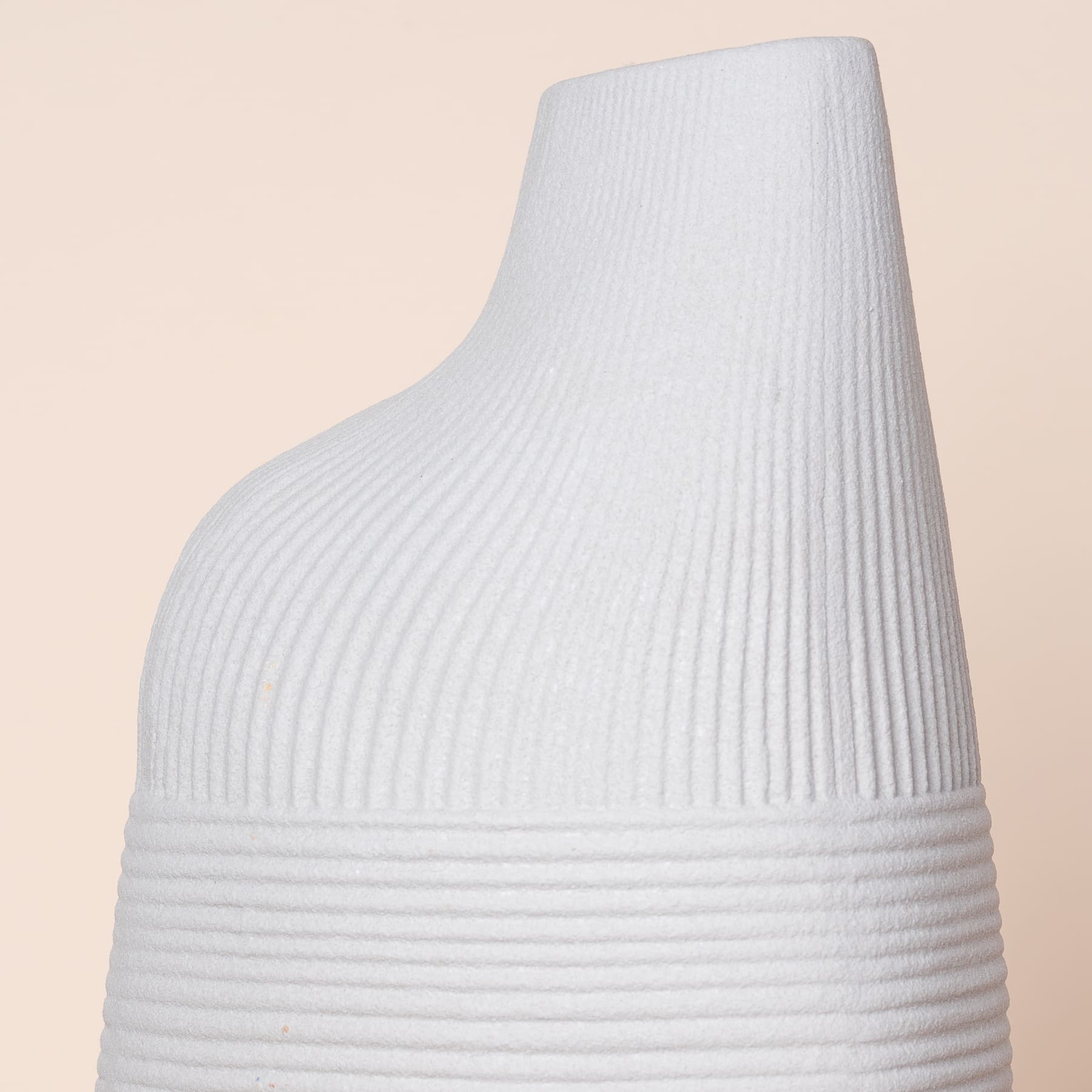 Eine weiße, gerippte Keramikvase oder ein Gefäß mit hoher, konischer Form und glatter, gleichmäßiger Oberfläche vor einem hellen, neutralen Hintergrund.