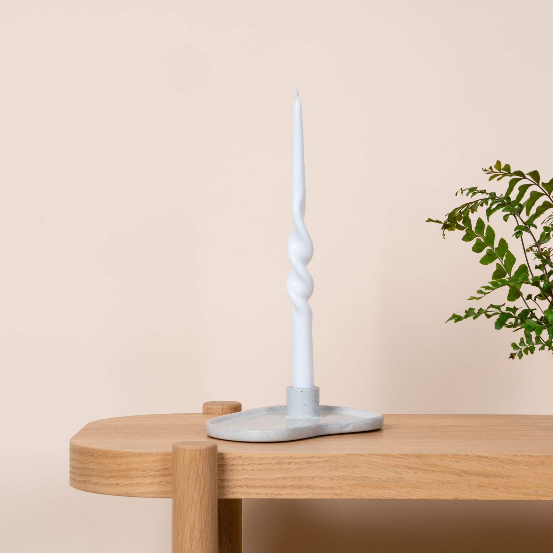 Auf einem Holztisch steht eine weiße Spiralkerze, im Hintergrund eine Topfpflanze.