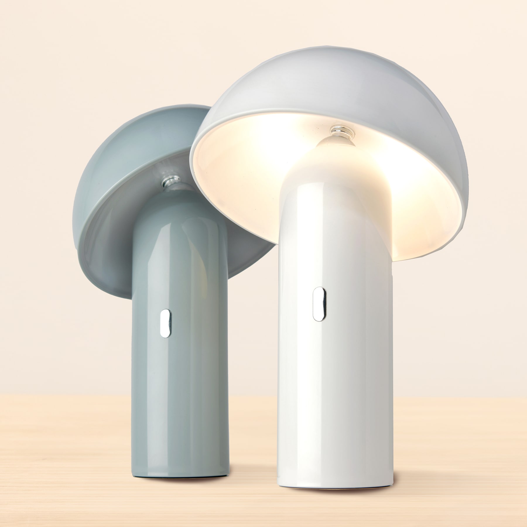 Zwei moderne, minimalistische Tischlampen mit abgerundeten, kuppelförmigen Schirmen in Hellgrau und Weiß auf neutralem Beige.