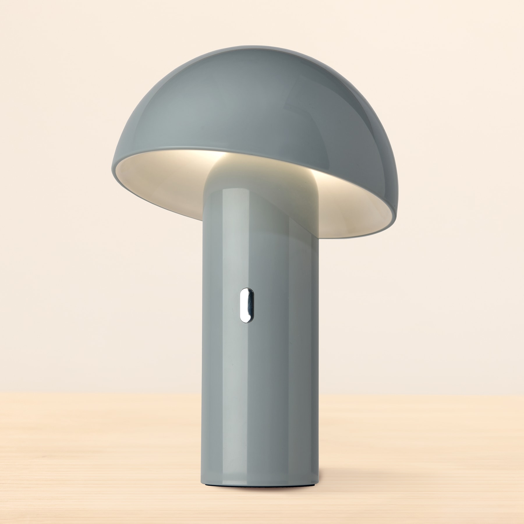 Eine graue, kuppelförmige Lampe mit zylindrischem Sockel sitzt auf einer hellen Oberfläche.