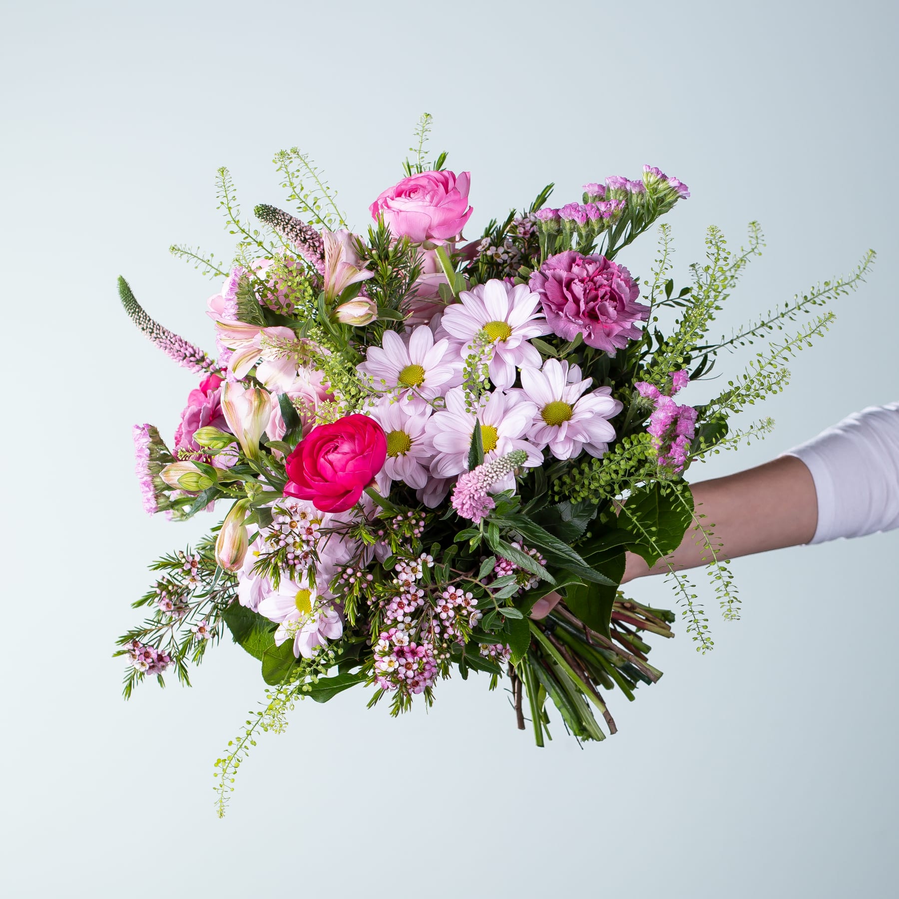 Ein leuchtender Strauß rosa und weißer Blumen, darunter Rosen, Gänseblümchen und andere Blüten, den eine Person vor einem schlichten hellen Hintergrund in den Händen hält.