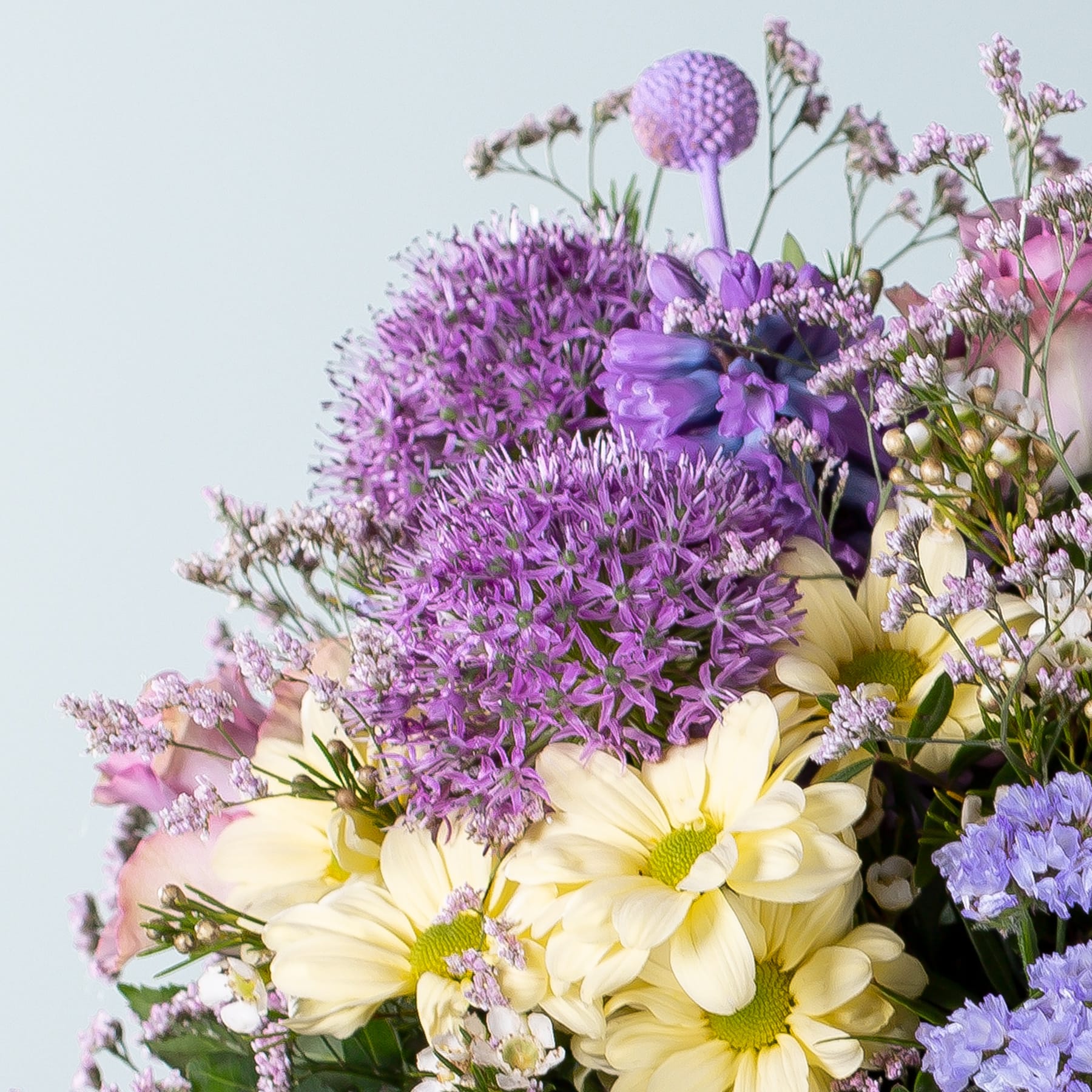 Ein lebendiger Strauß aus lila Alliumblüten, gelben Gänseblümchen und anderen bunten Blüten vor einem weichen, dunstigen Hintergrund.