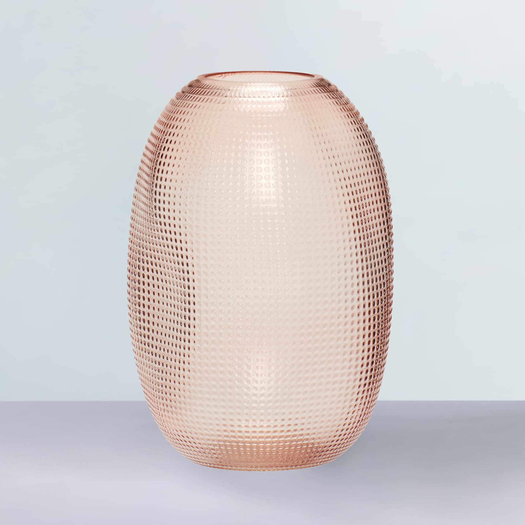 Eine roségoldfarbene Glasvase mit strukturierter, gemusterter Oberfläche steht auf einem schlichten, hellen Hintergrund.