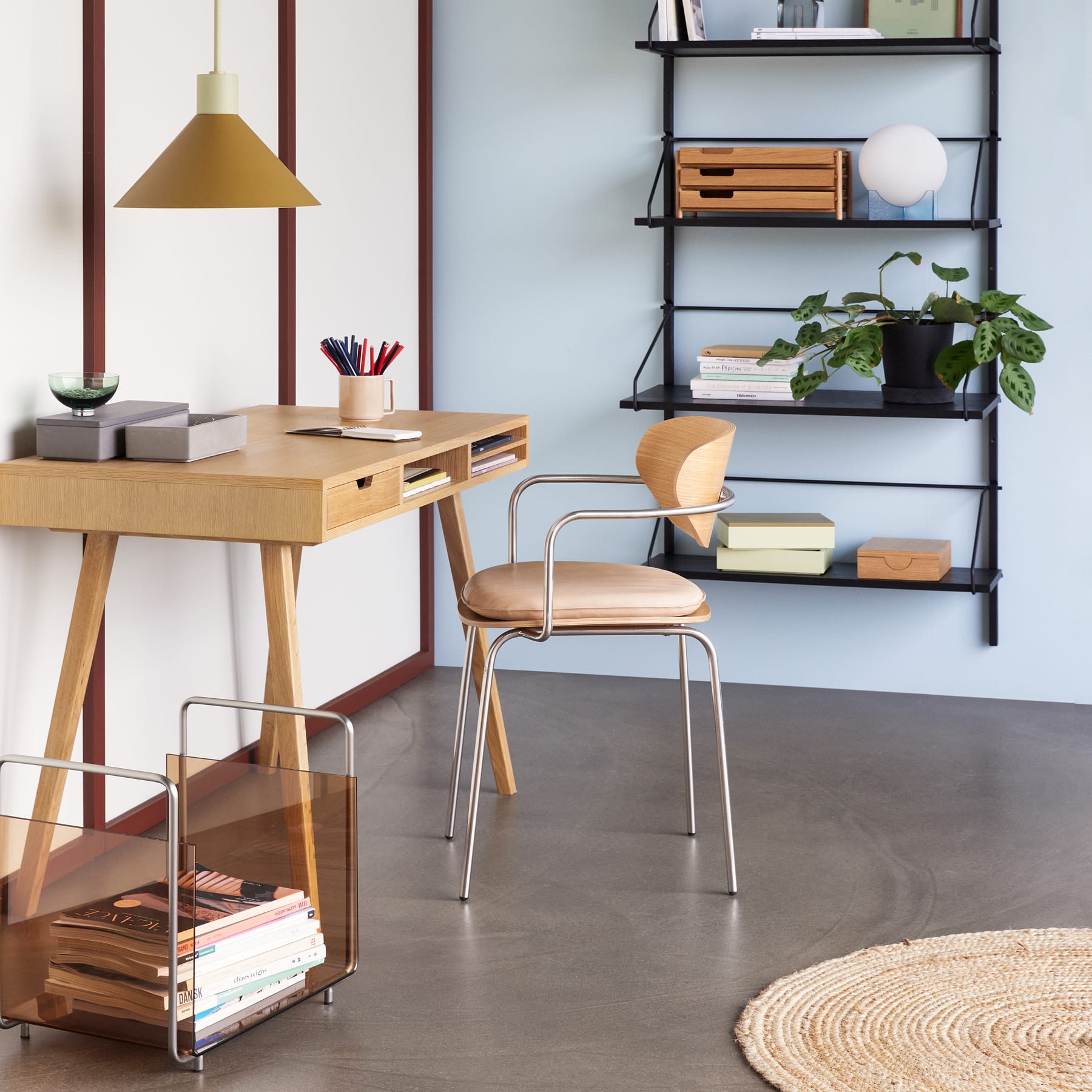 Ein gemütlicher und gut organisierter Home-Office-Bereich mit einem Holzschreibtisch, einer gelben Hängelampe und einem Metallregal mit verschiedenen dekorativen und funktionalen Gegenständen.