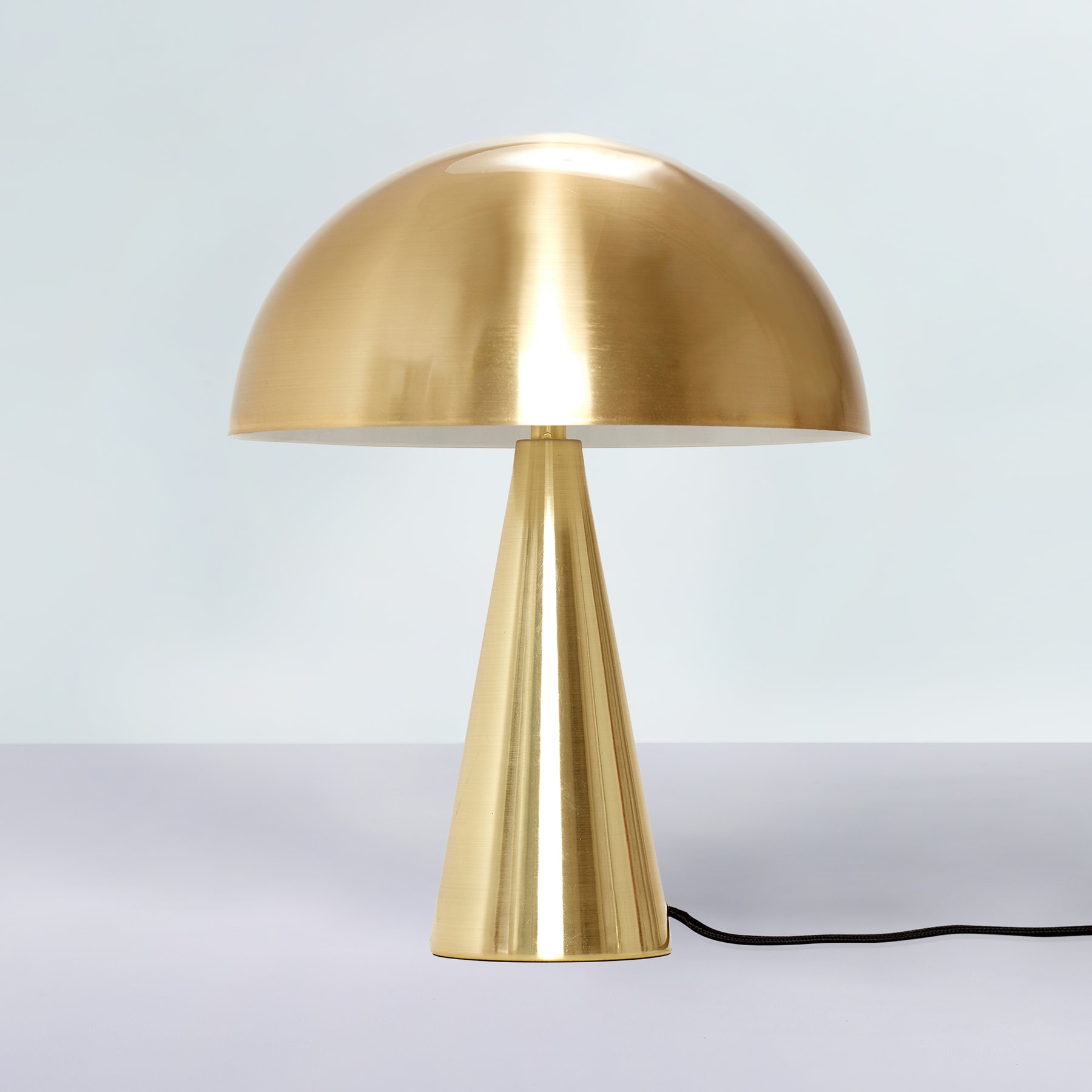 Eine goldene, kuppelförmige Lampe mit einem hohen, konischen Sockel steht auf einer schlichten, hellen Oberfläche vor einem neutralen Hintergrund.
