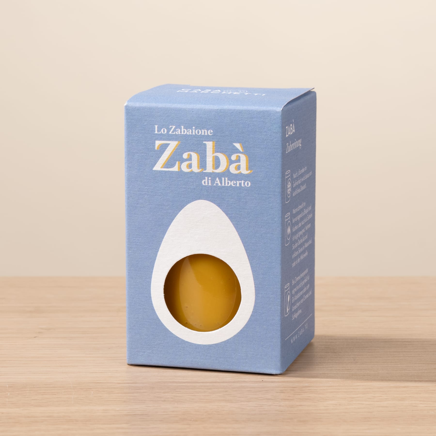 Ein blauer Karton mit dem Text „Zaba di Alberto“ und einem gelben Gegenstand darin, der auf einer Holzoberfläche ruht.