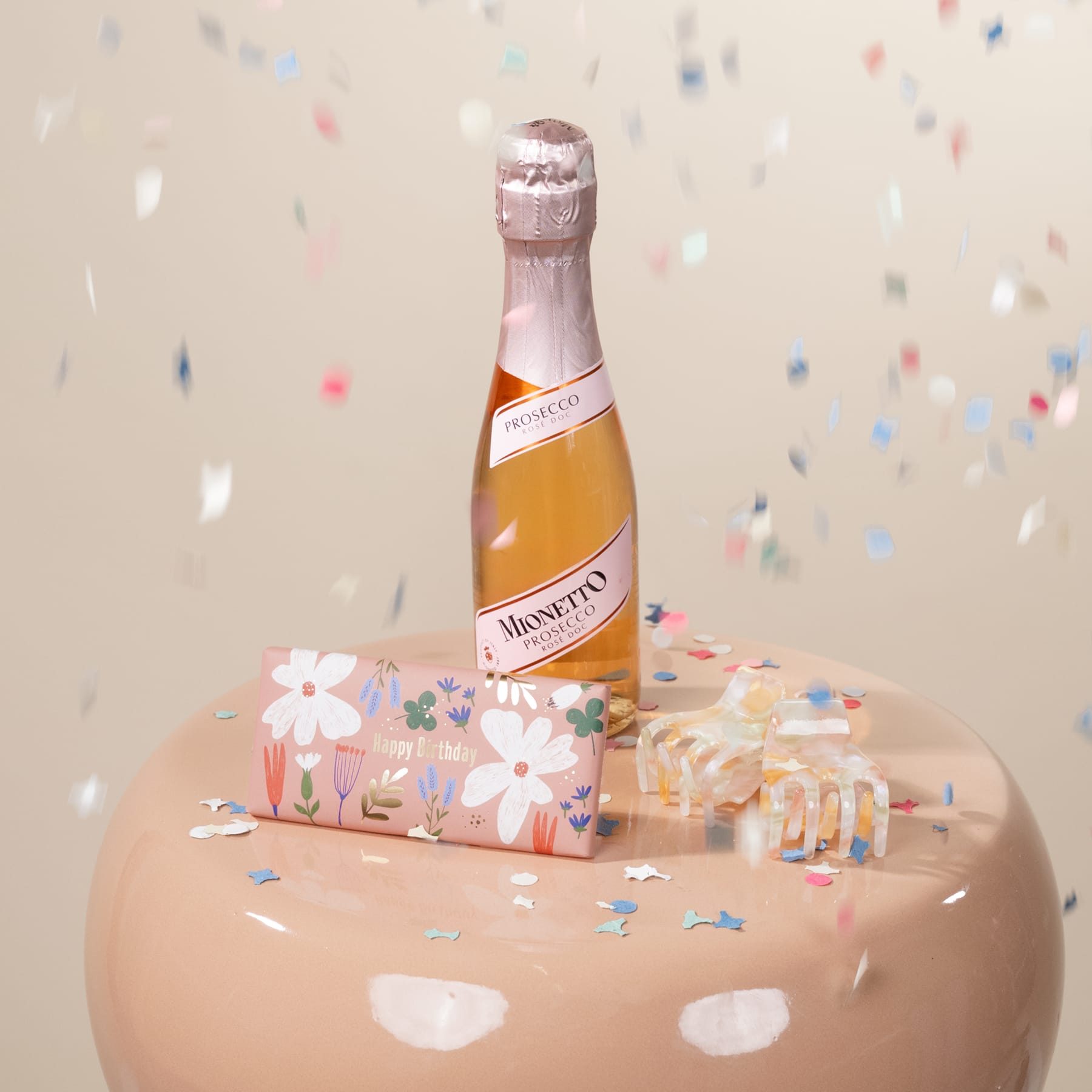Eine Flasche Sekt Martini Asti steht auf einem rosa Kuchen, der mit buntem Konfetti und Blumenmustern verziert ist.