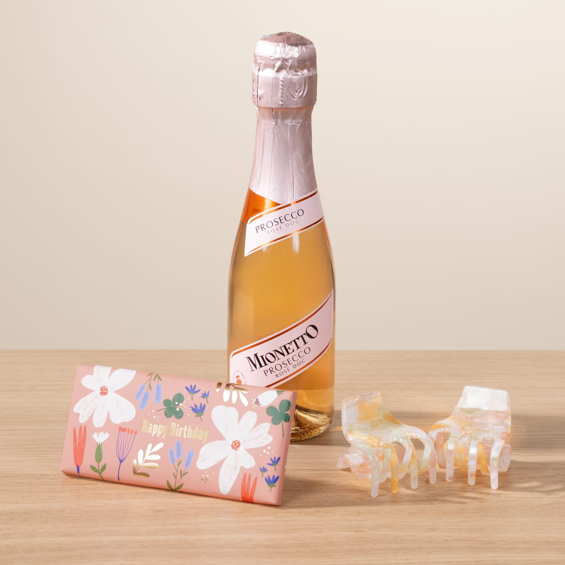 Eine Flasche Sekt, umgeben von einer farbenfrohen Geschenkbox mit Blumenmuster und dekorativen Papierausschnitten, steht auf einer Holzoberfläche.
